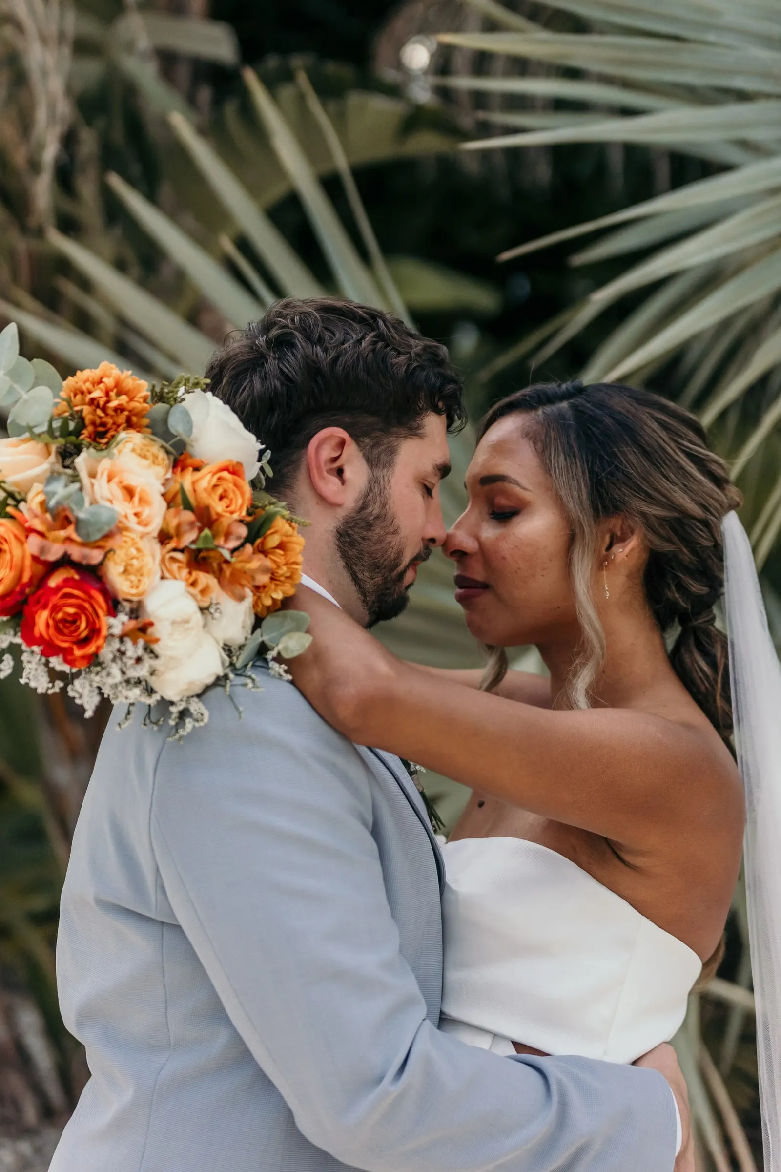 Close embrace of the couple, nose to nose, with the bouquet over his shoulder