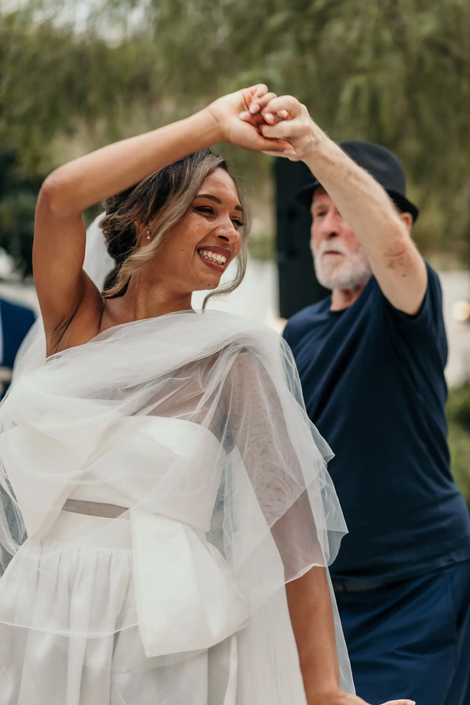 Bride in a tulle wrap twirling with the man in the black hat