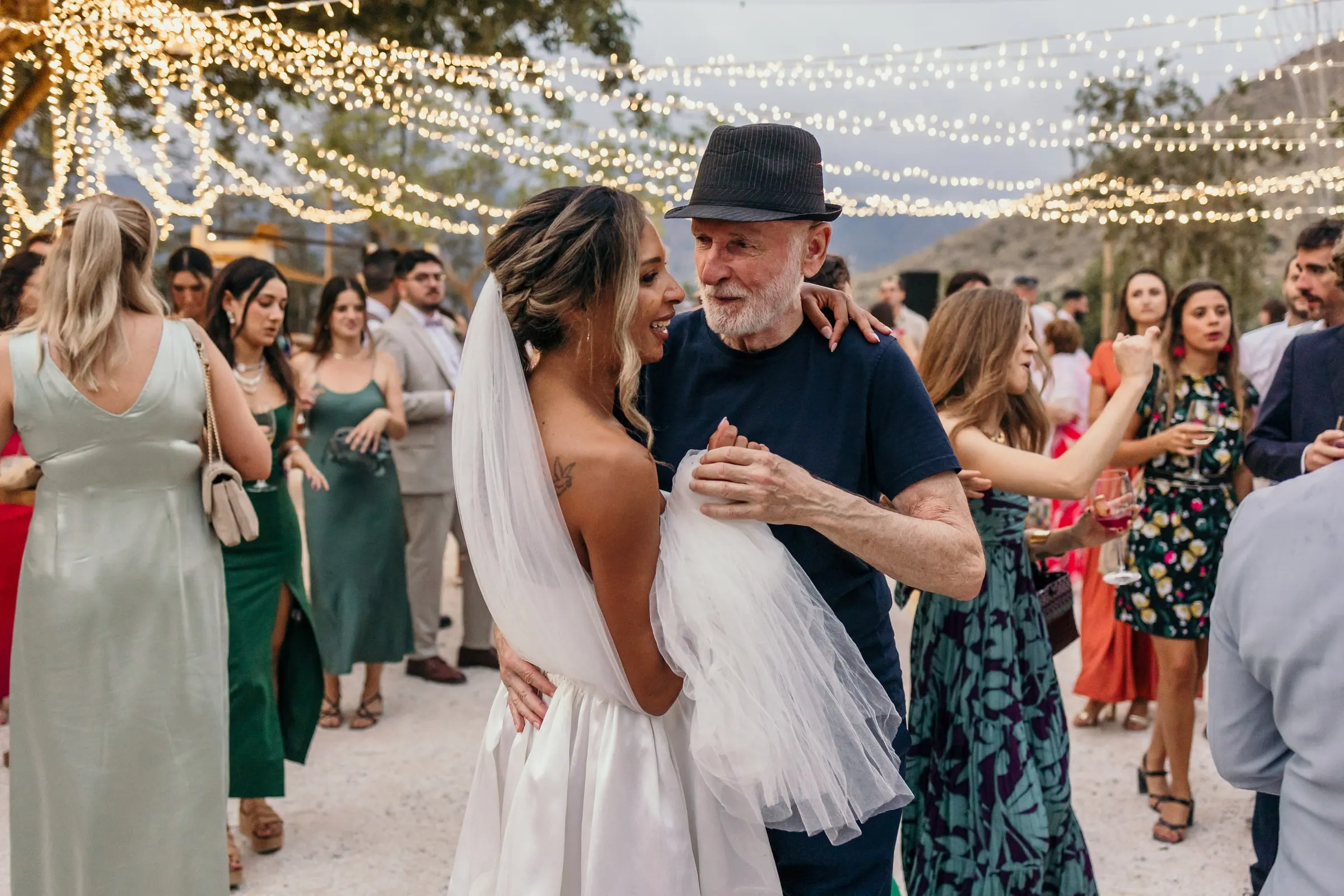 Bride laughing in a dance with the man in the black hat under the lights