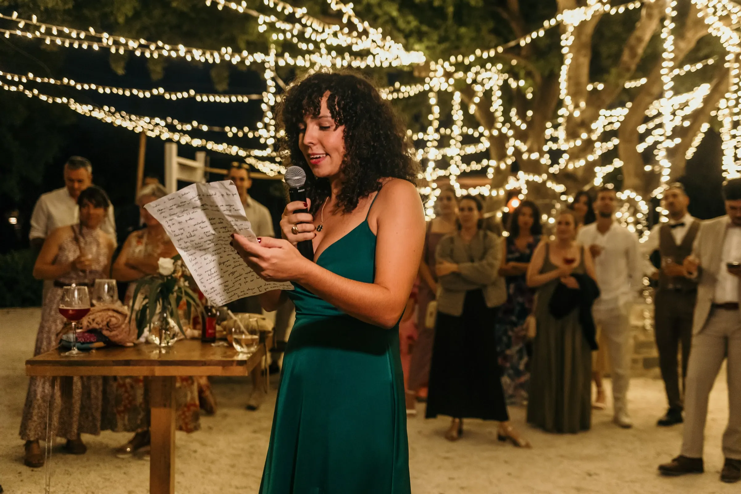 Bridesmaid in green giving a speech from a printed page under the fairy lights