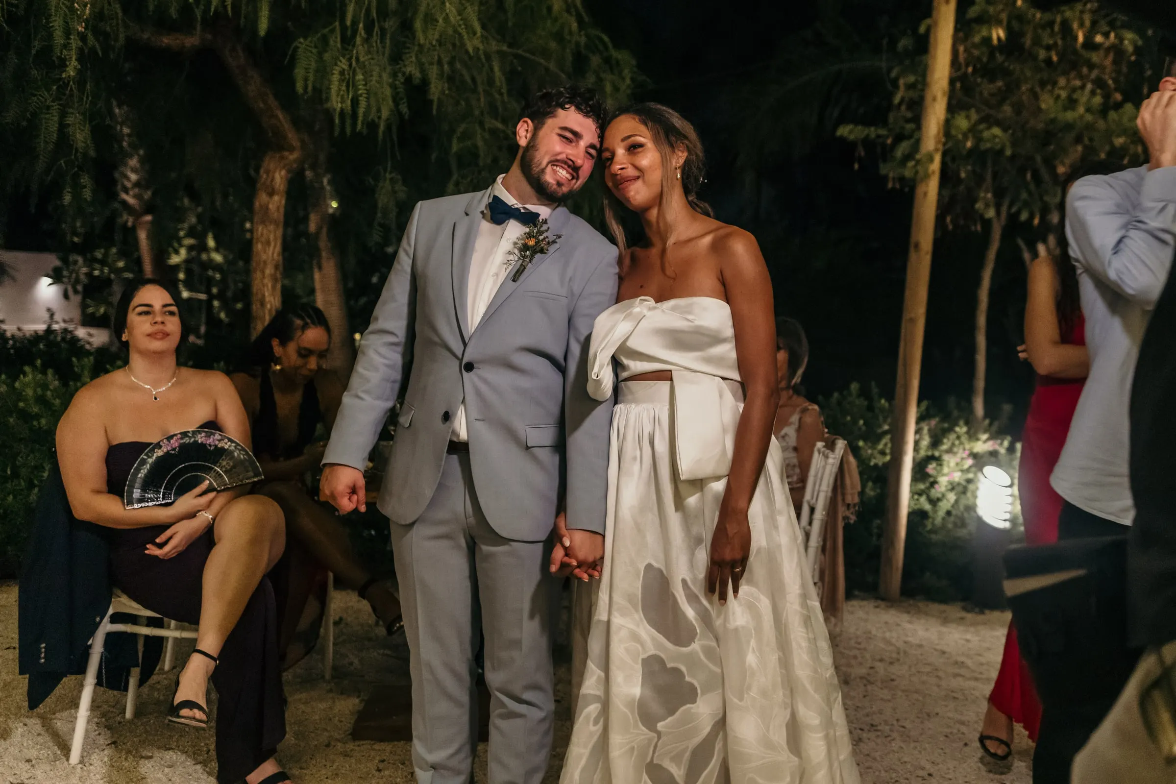 Bride and groom arm in arm among the guests at night in the garden