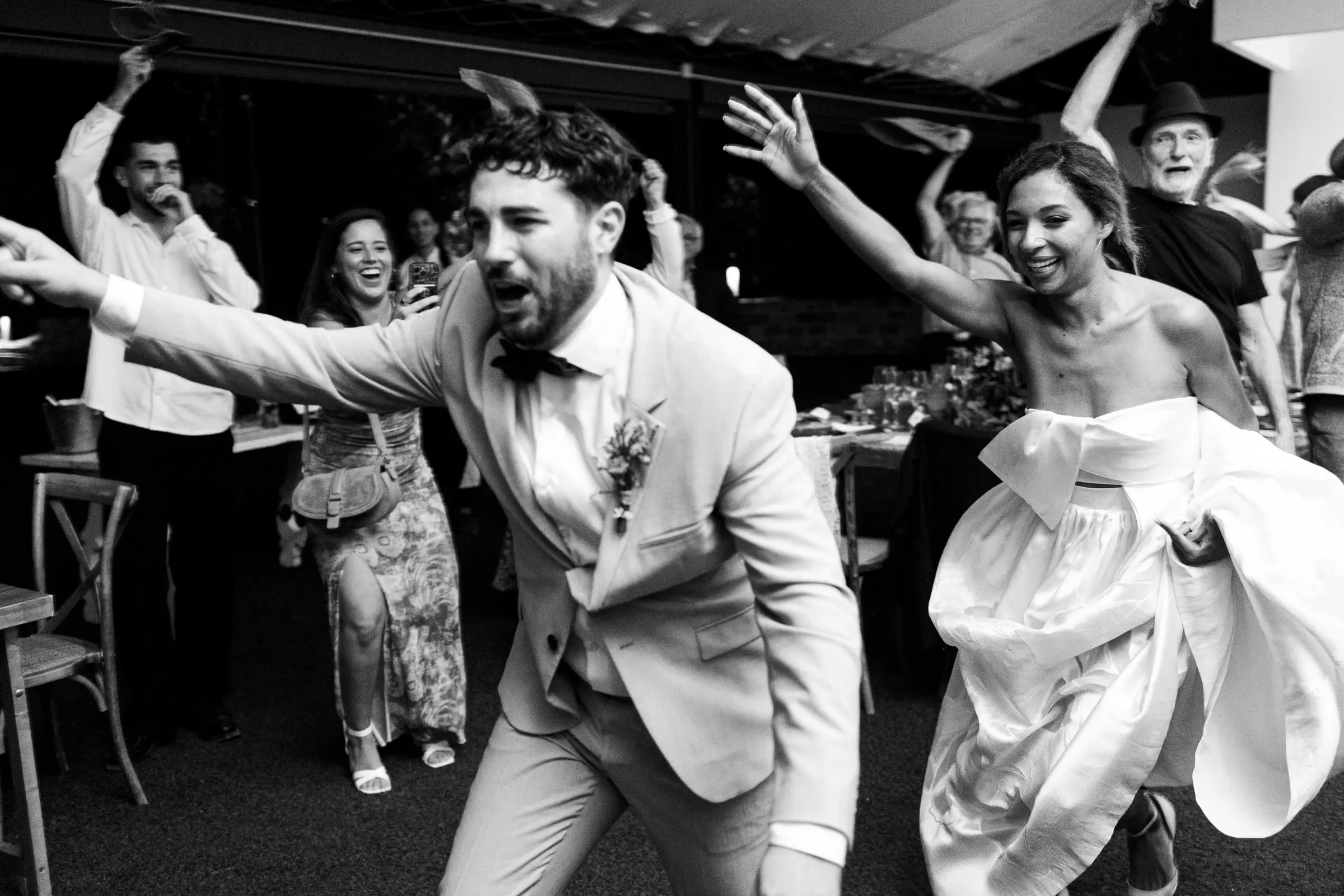 Black and white photo of the bride and groom dancing wildly with their guests