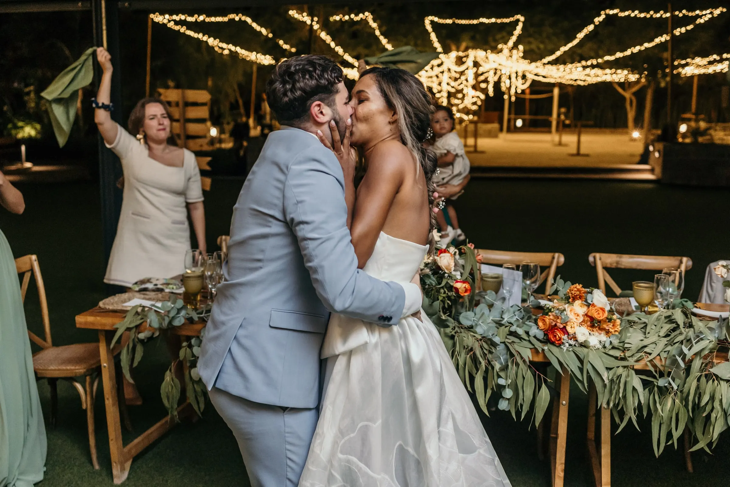Couple kissing beside the long dinner table dressed with greenery and orange flowers