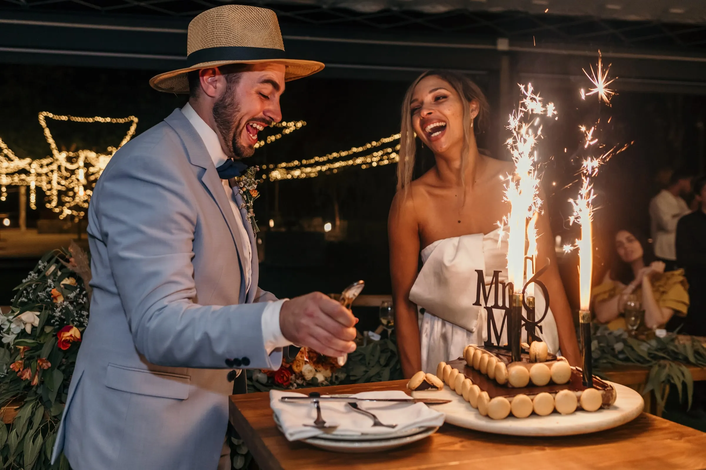 Bride and groom laughing as they cut a cake with sparklers and a Mr & Mrs topper