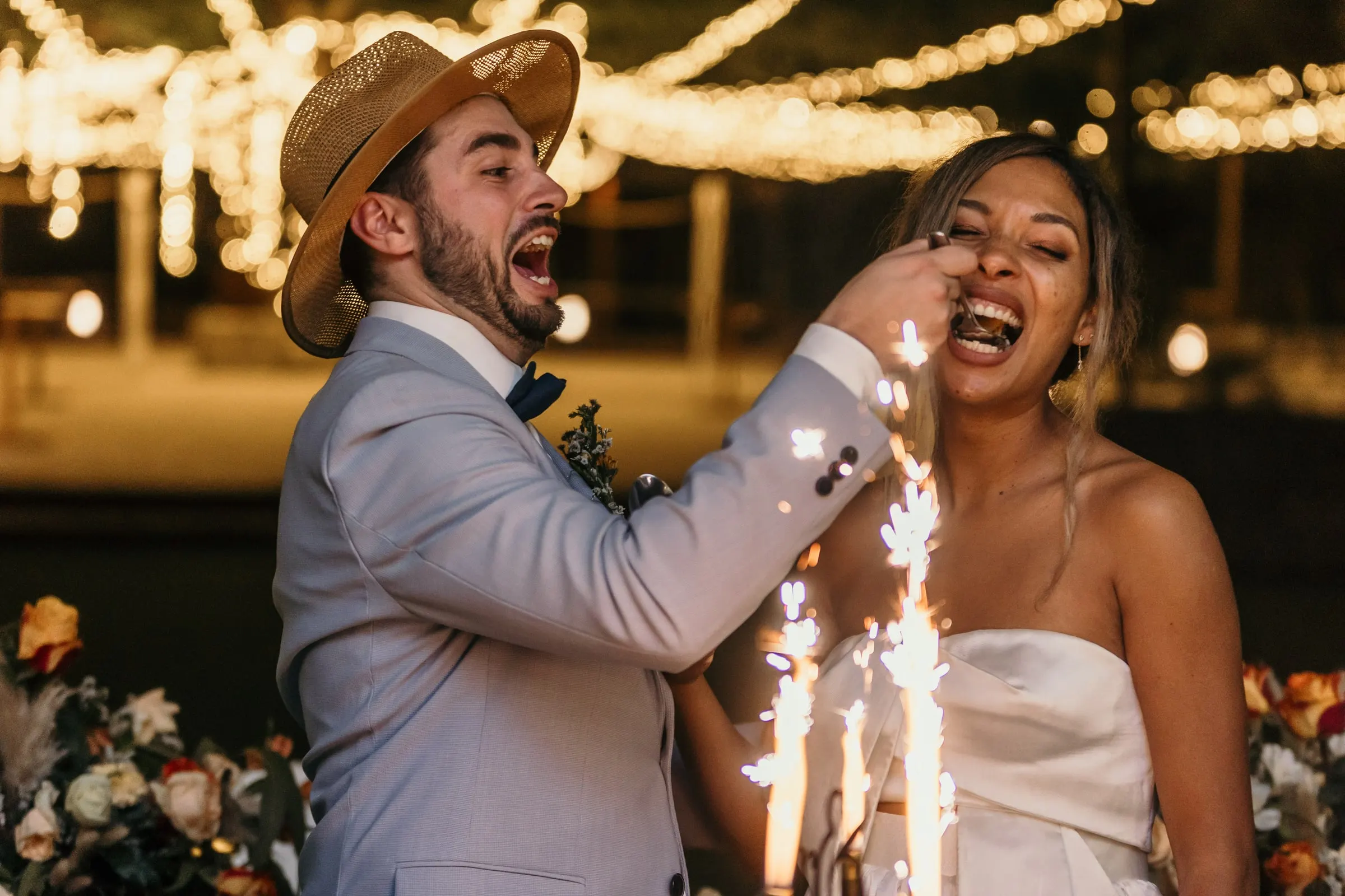 Bride feeding the groom a piece of cake as he bursts out laughing