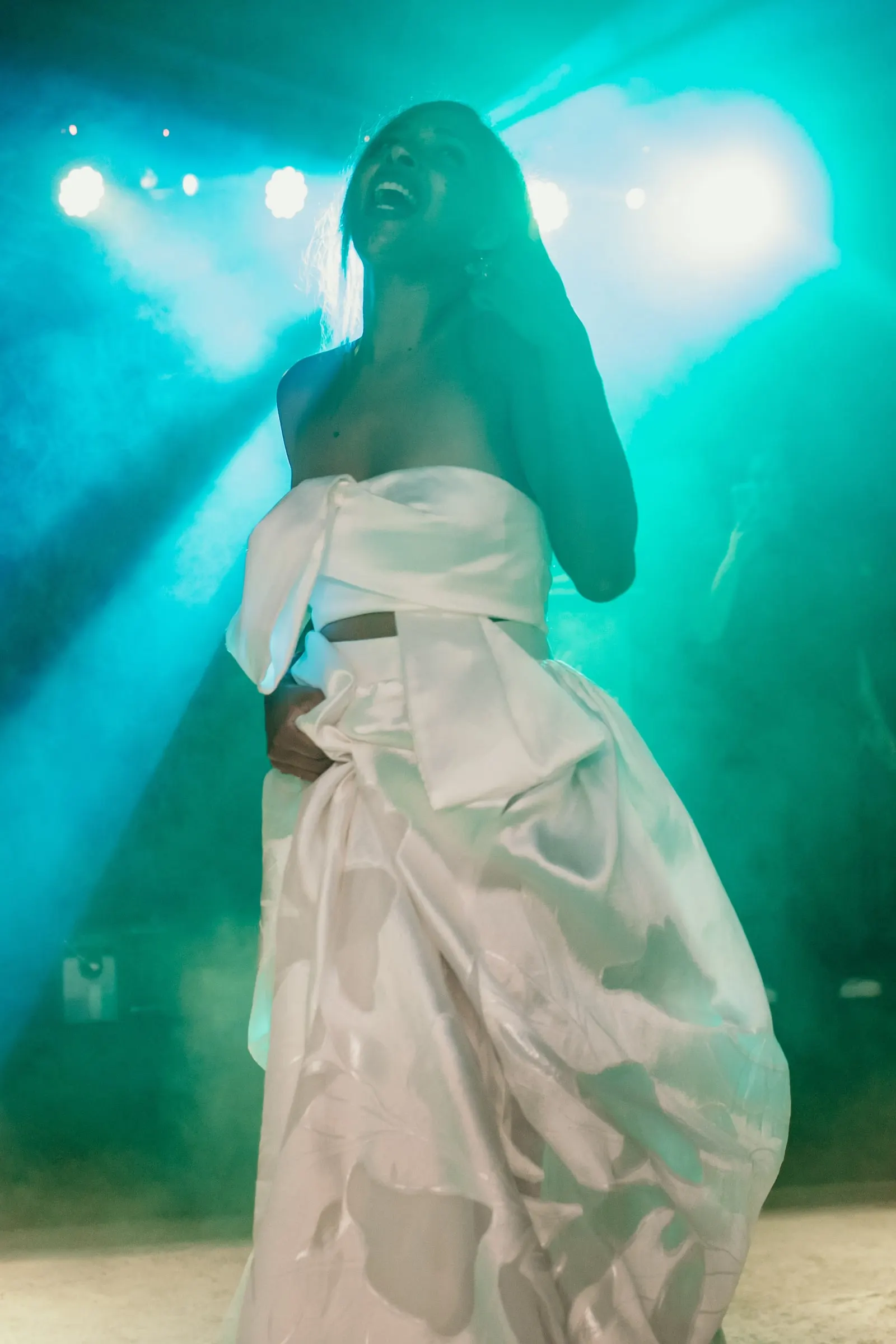 Bride laughing with her eyes closed in turquoise light on the dance floor