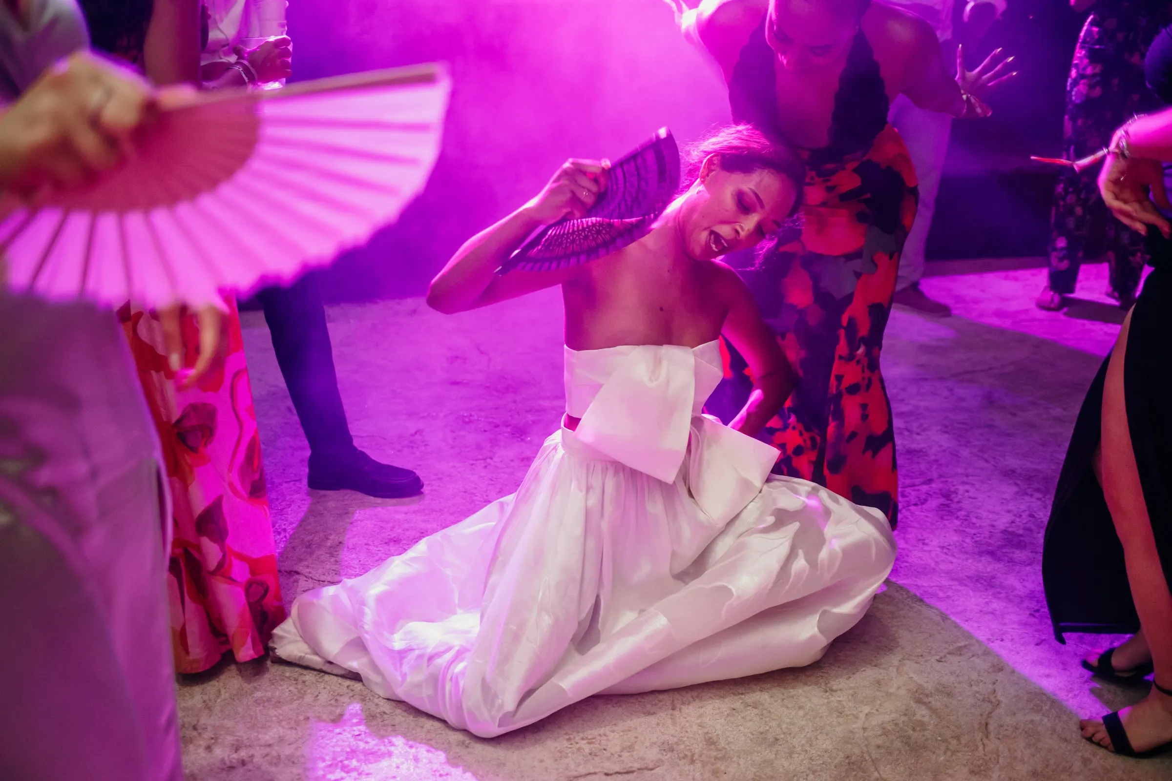 Bride dancing on the floor as a guest waves a pink fan in magenta light