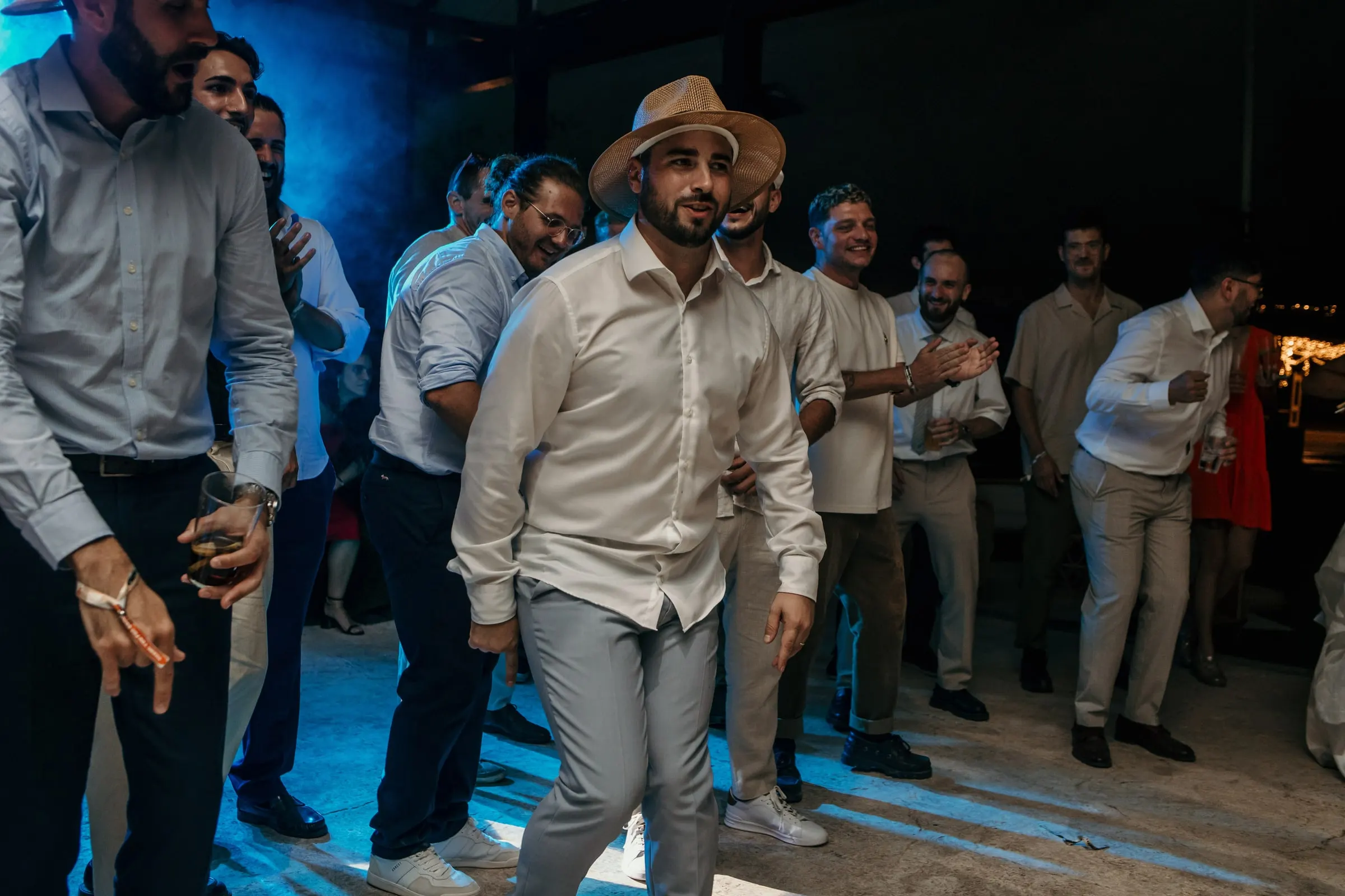 Groom's friends in white shirts and straw hats dancing in blue light