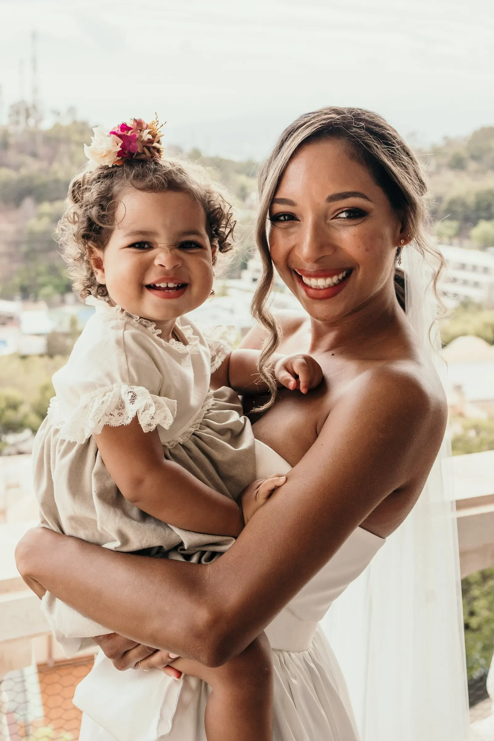 Bride smiling cheek to cheek with the little girl in her arms on the villa balcony, Finca Botania, Málaga