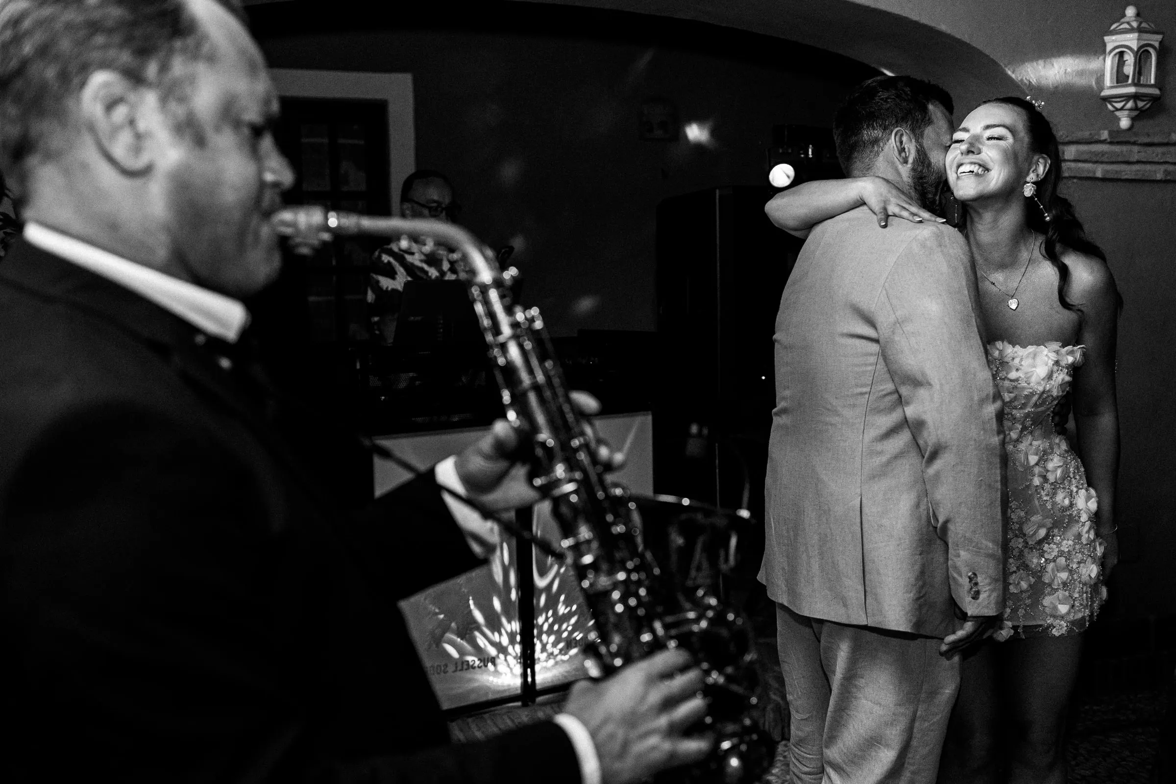 Black and white of the bride hugging the groom on the dance floor while a saxophonist plays, Hacienda San José, Mijas