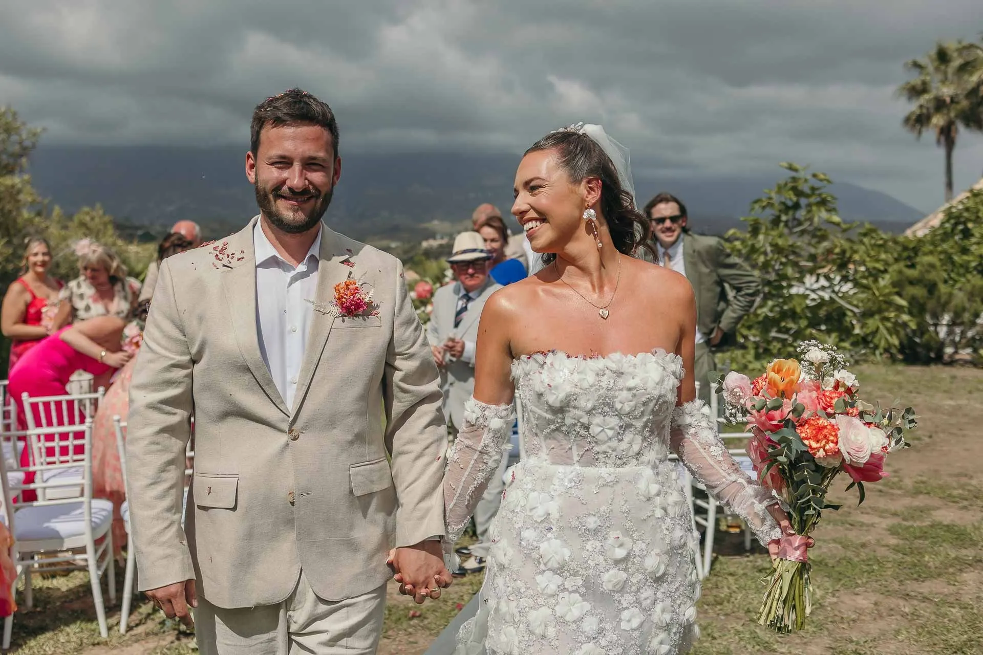 Bride and groom walk back down the aisle hand in hand, smiling, guests in pink behind, Hacienda San José, Mijas