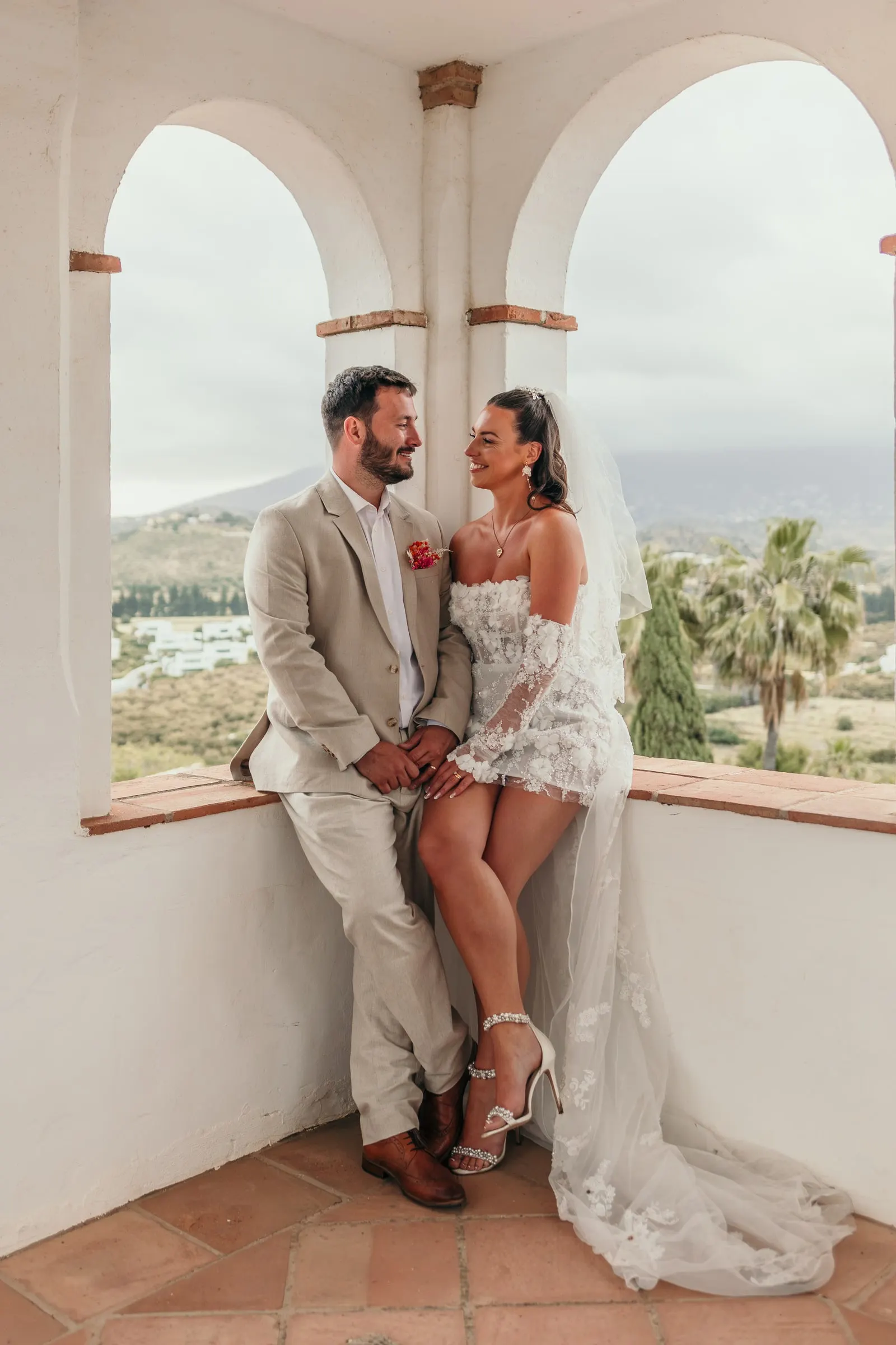 Bride and groom sitting together in an arched window seat above the valley, Hacienda San José, Mijas