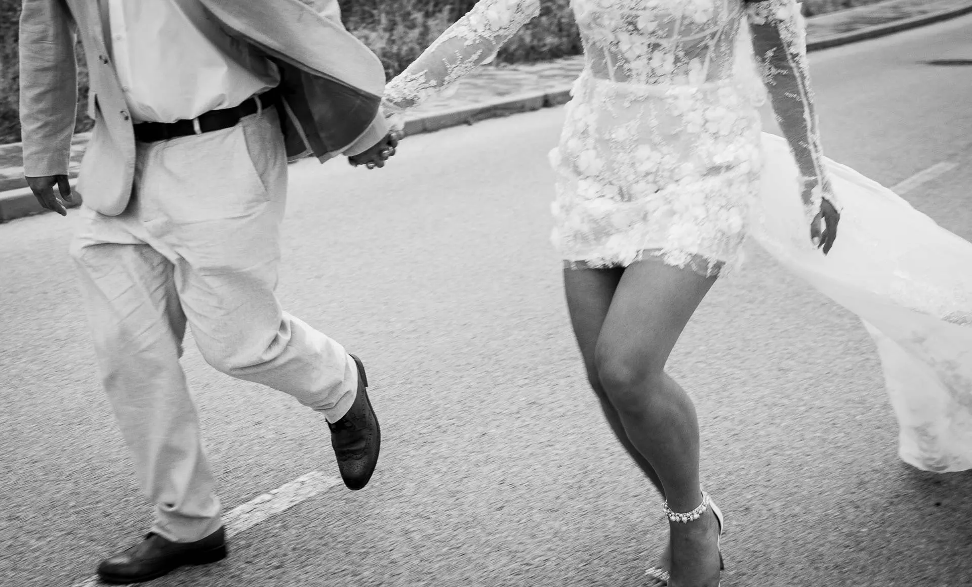 Black and white close-up of the couple's legs as they stride hand in hand along the road, Hacienda San José, Mijas