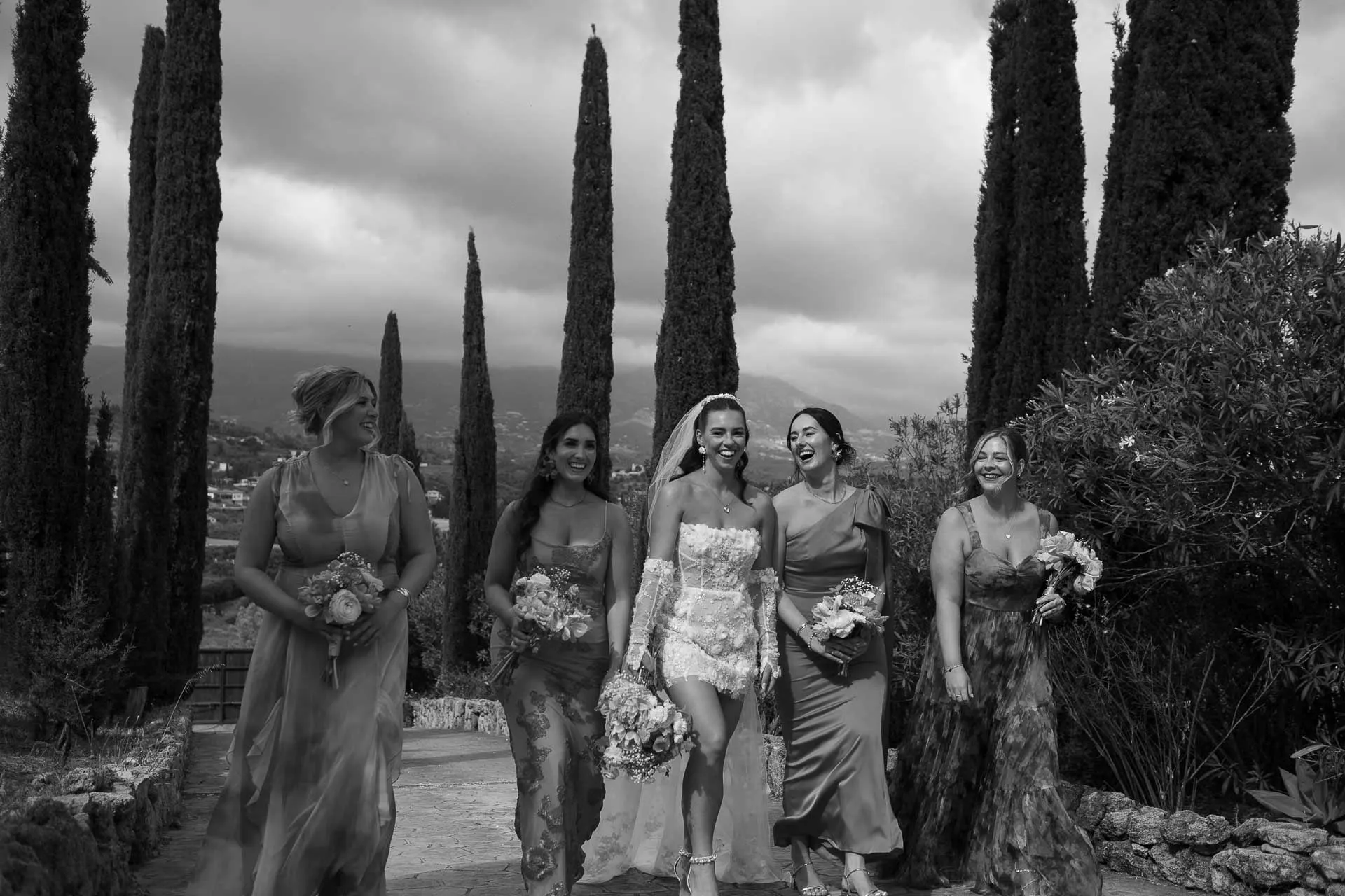 Black and white of the bride walking with her bridesmaids among tall cypress trees, Hacienda San José, Mijas