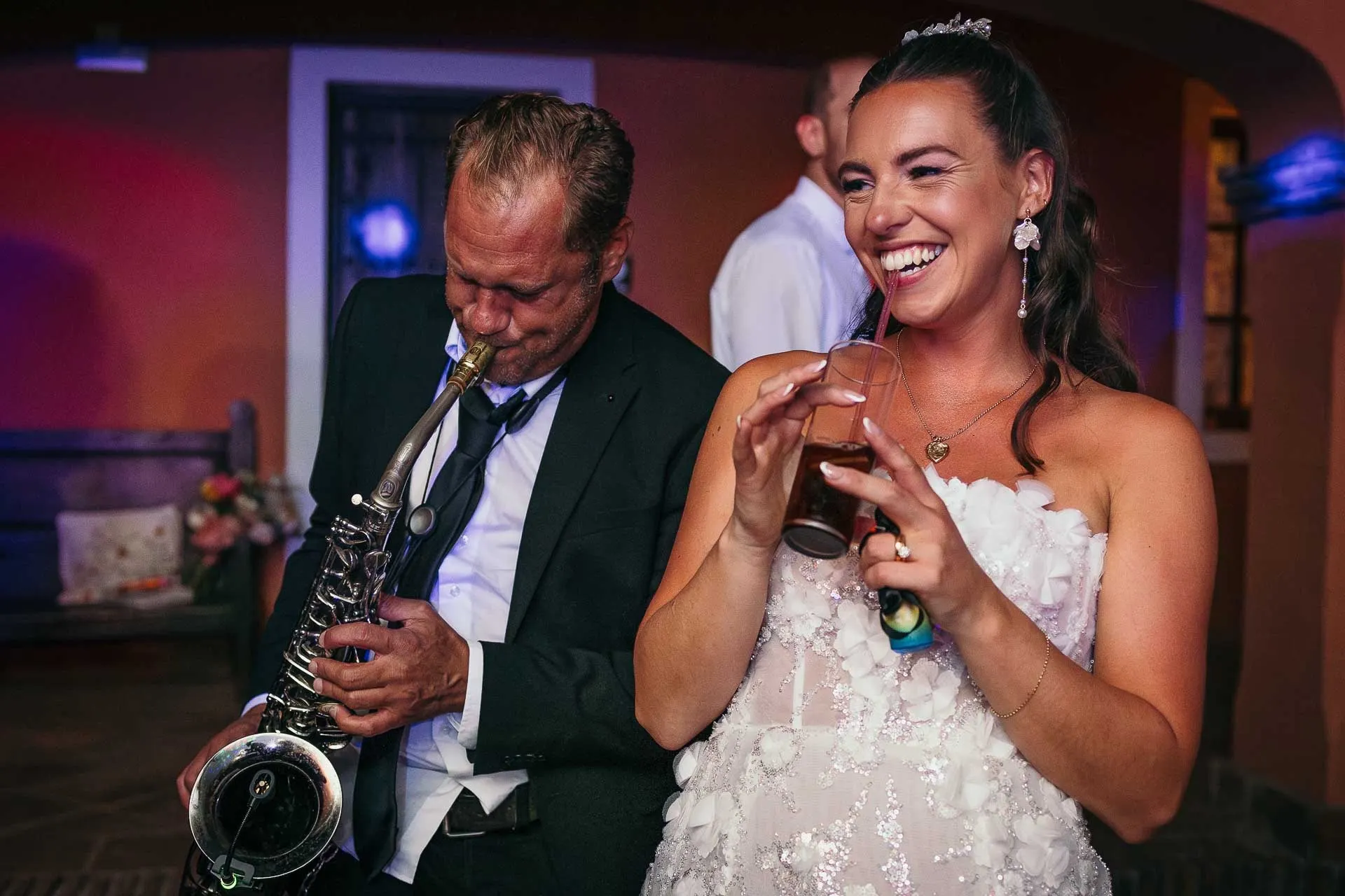 Bride laughing with a drink in hand beside the saxophonist during the party, Hacienda San José, Mijas