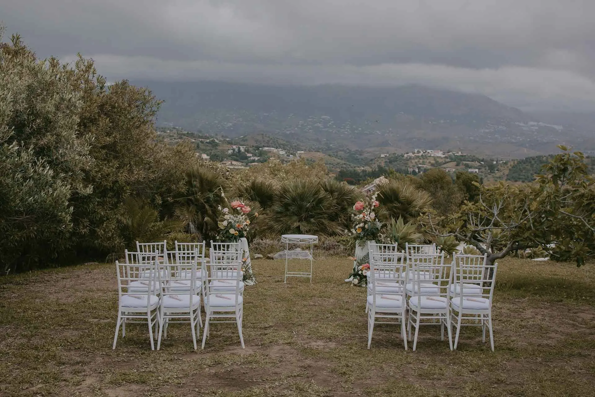 Empty white ceremony chairs on the lawn among olive trees, mountains behind, Hacienda San José, Mijas