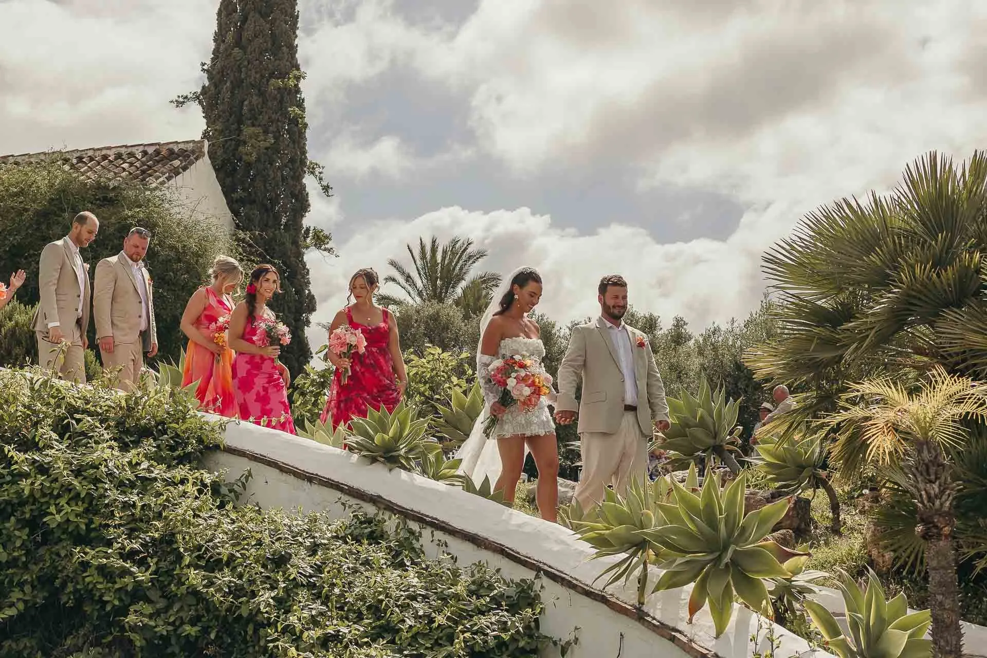 Wedding party walking along a white garden wall among palms and cypresses, Hacienda San José, Mijas