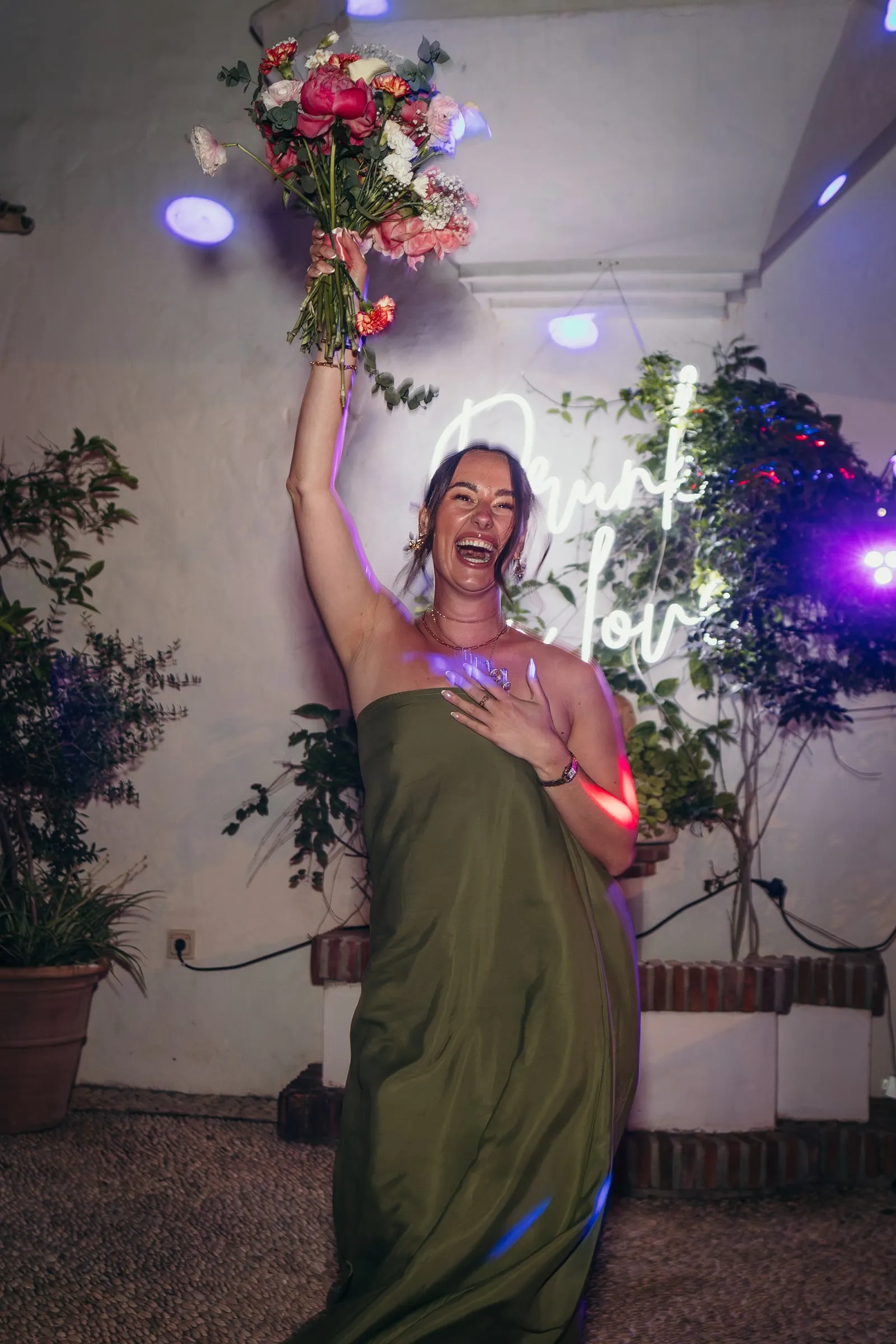 Guest in a green dress laughing as she raises the caught bouquet at the party, Hacienda San José, Mijas