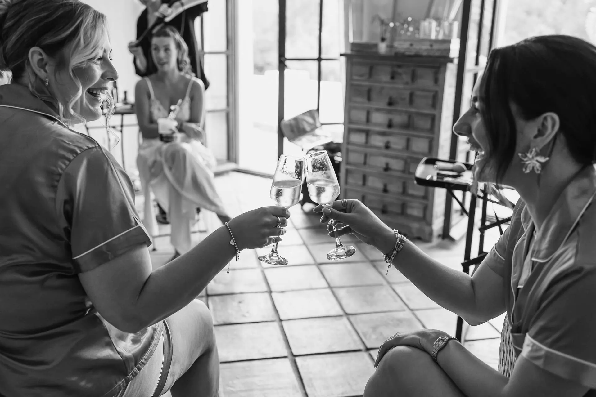 Black and white of two women in robes clinking glasses of cava while getting ready, Hacienda San José, Mijas