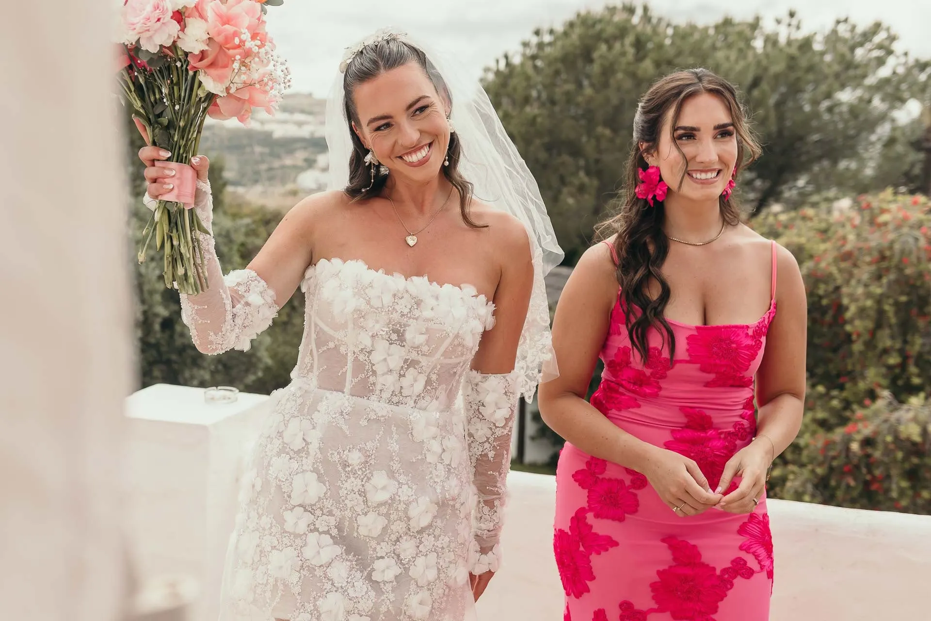 Bride waving her bouquet beside a smiling bridesmaid in a pink floral dress, Hacienda San José, Mijas