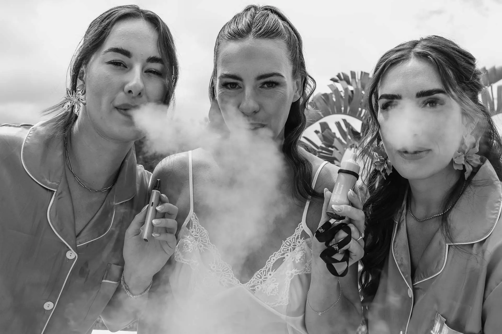 Black and white of the bride and two friends in pyjamas blowing out smoke and laughing, Hacienda San José, Mijas