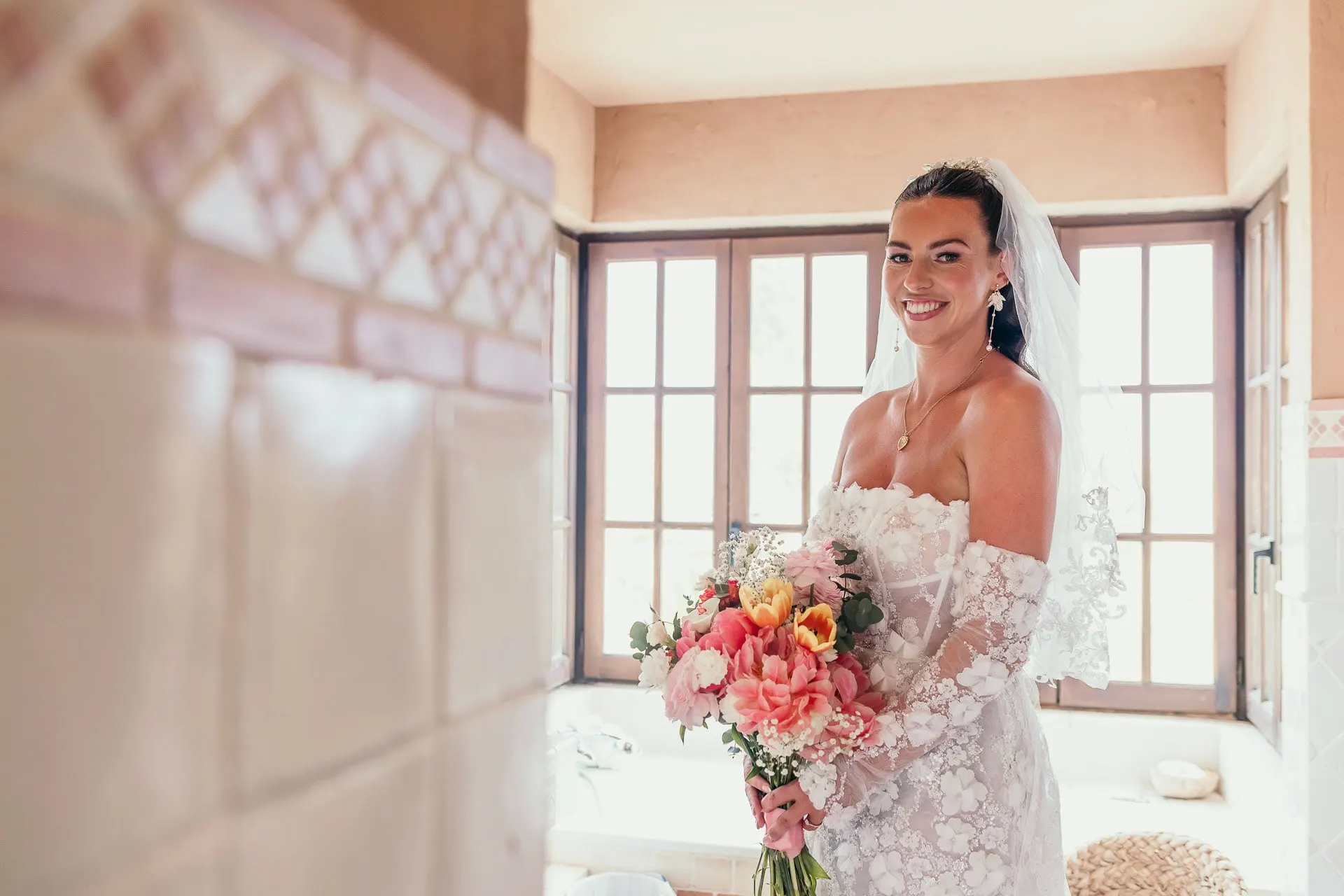 Bride holding her coral bouquet and smiling in a bright room with tiled walls, Hacienda San José, Mijas