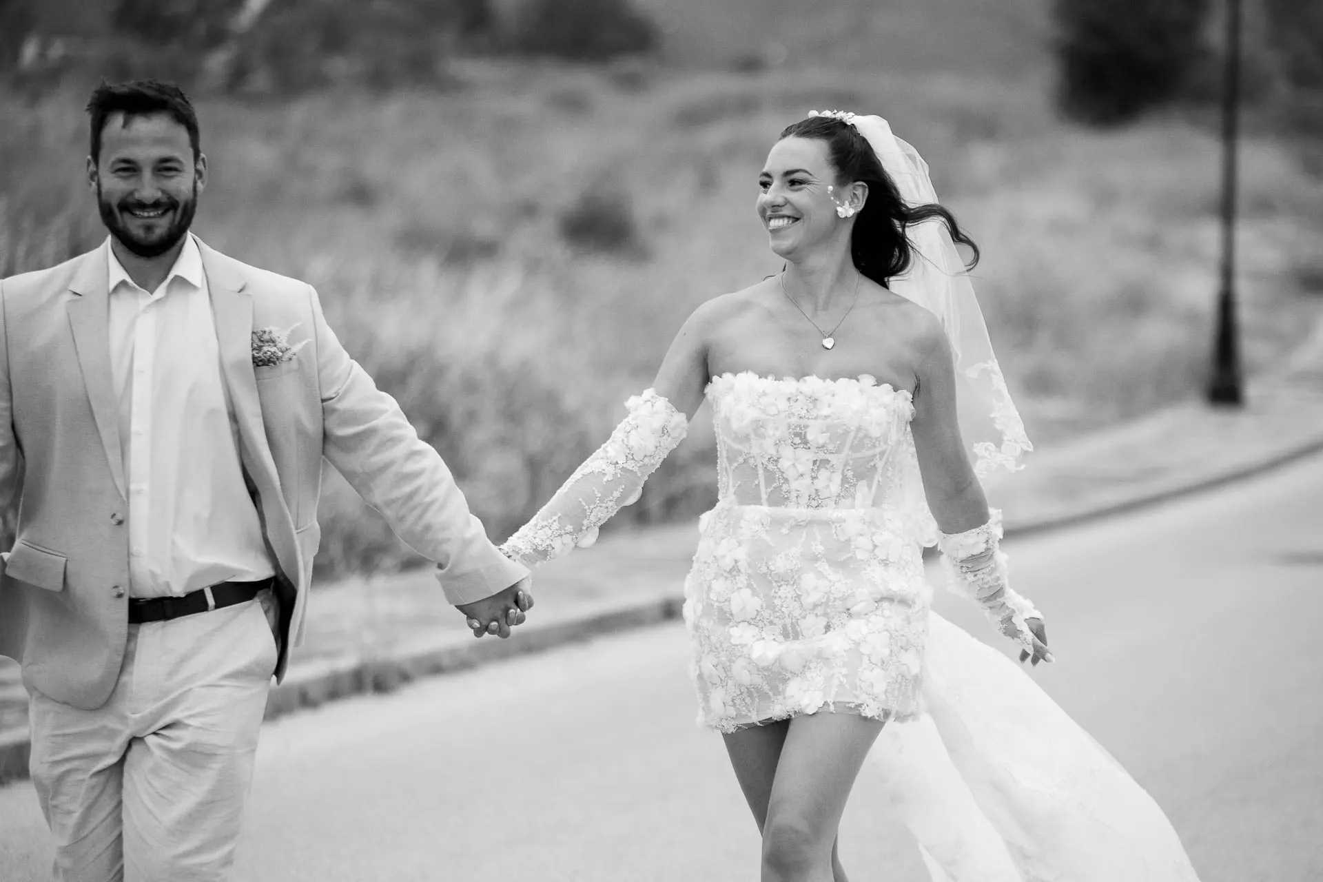 Black and white of the bride and groom running hand in hand along the road, laughing, Hacienda San José, Mijas