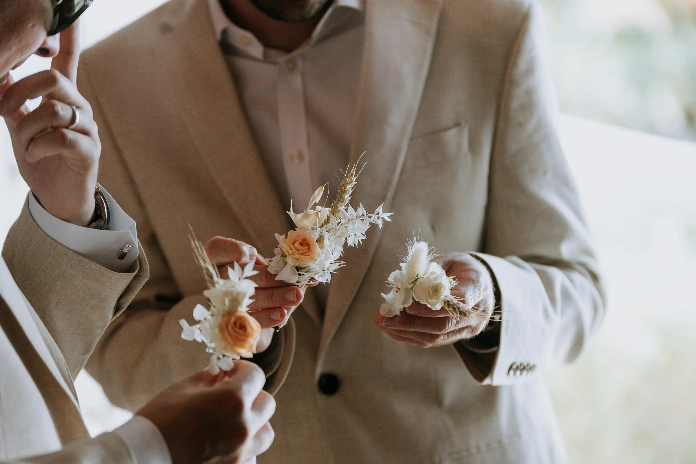Buttonholes of dried flowers and peach roses held against beige jackets, Hacienda San José