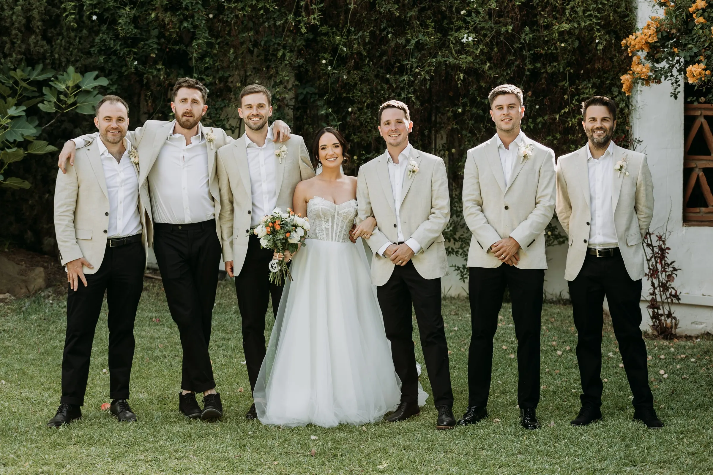 Bride and groom with the groomsmen in beige jackets on the lawn at Hacienda San José