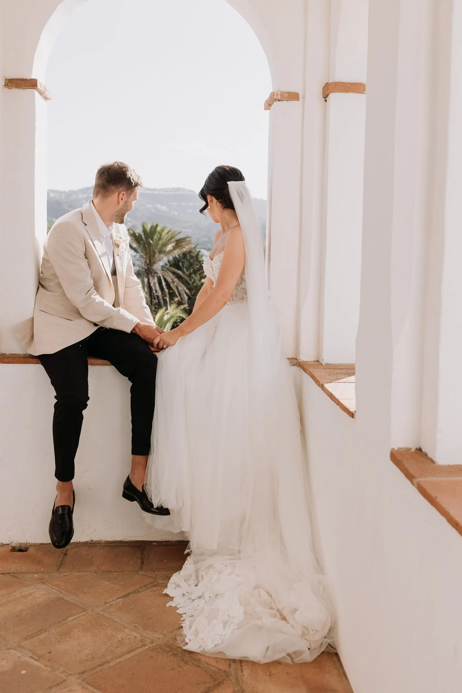 Groom sitting on the tower window holding the bride's hands, Mijas