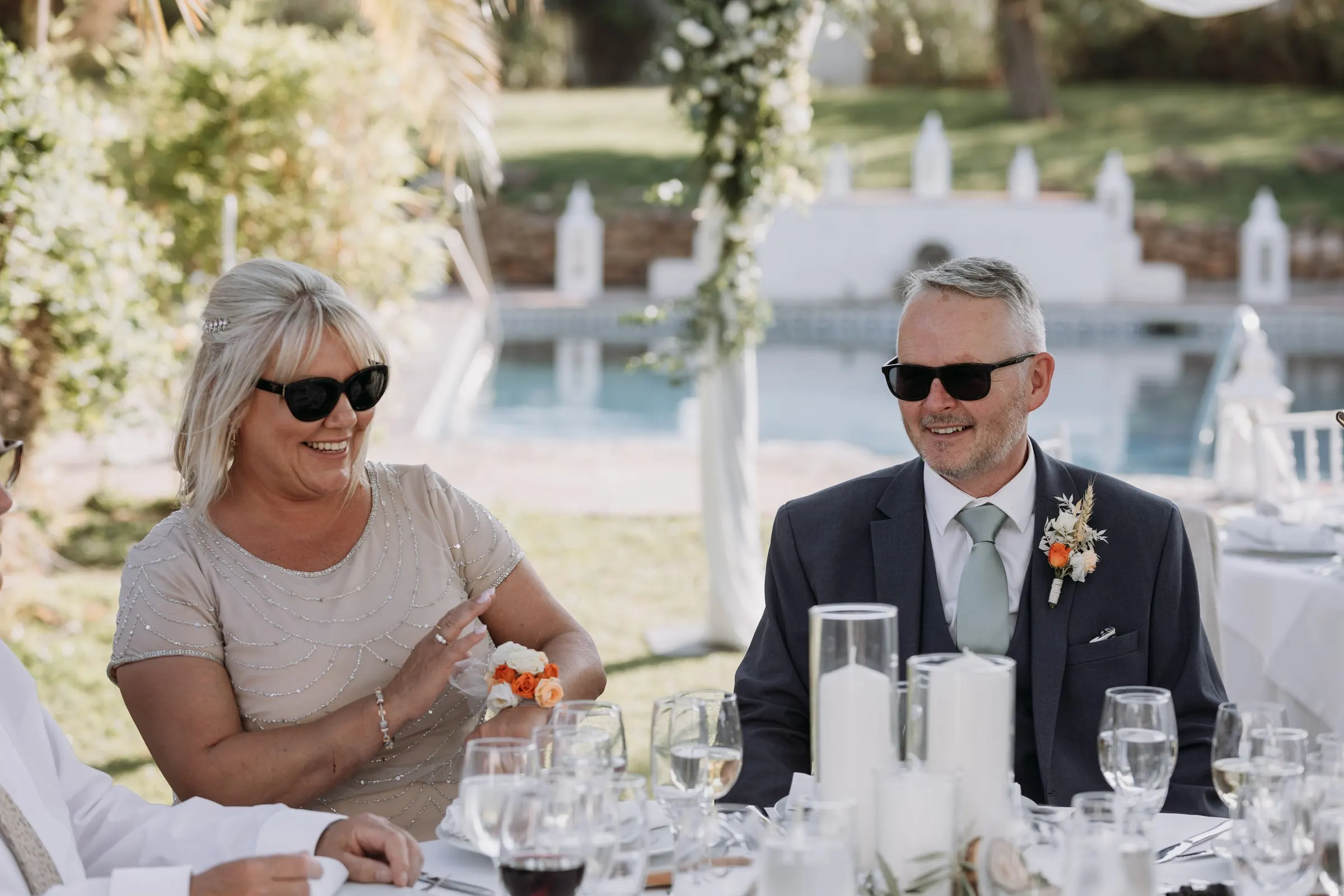 The bride's father laughing with a guest at a table by the pool, wedding lunch in Mijas