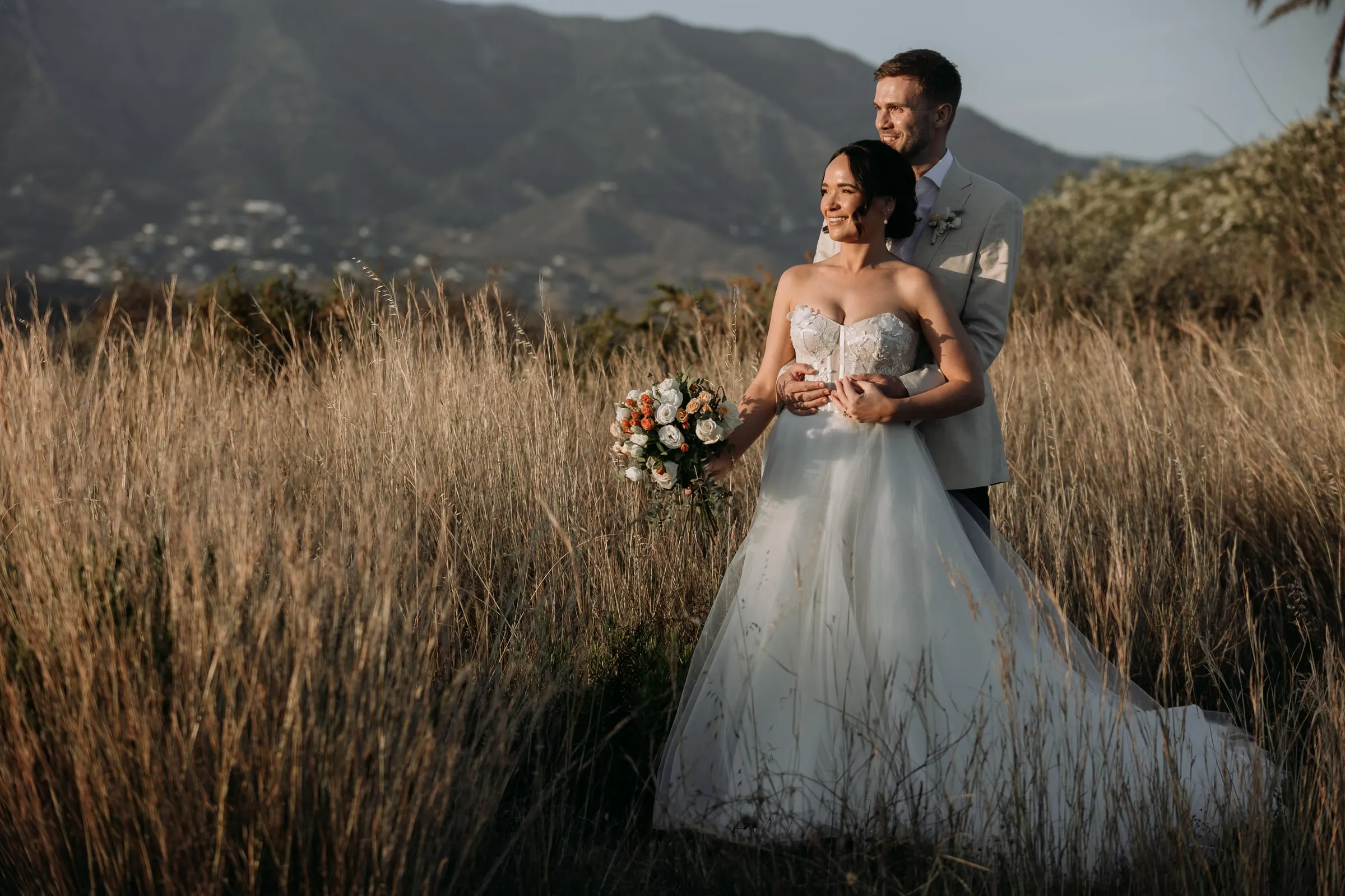 Bride and groom in the golden grass at sunset with the Sierra de Mijas behind