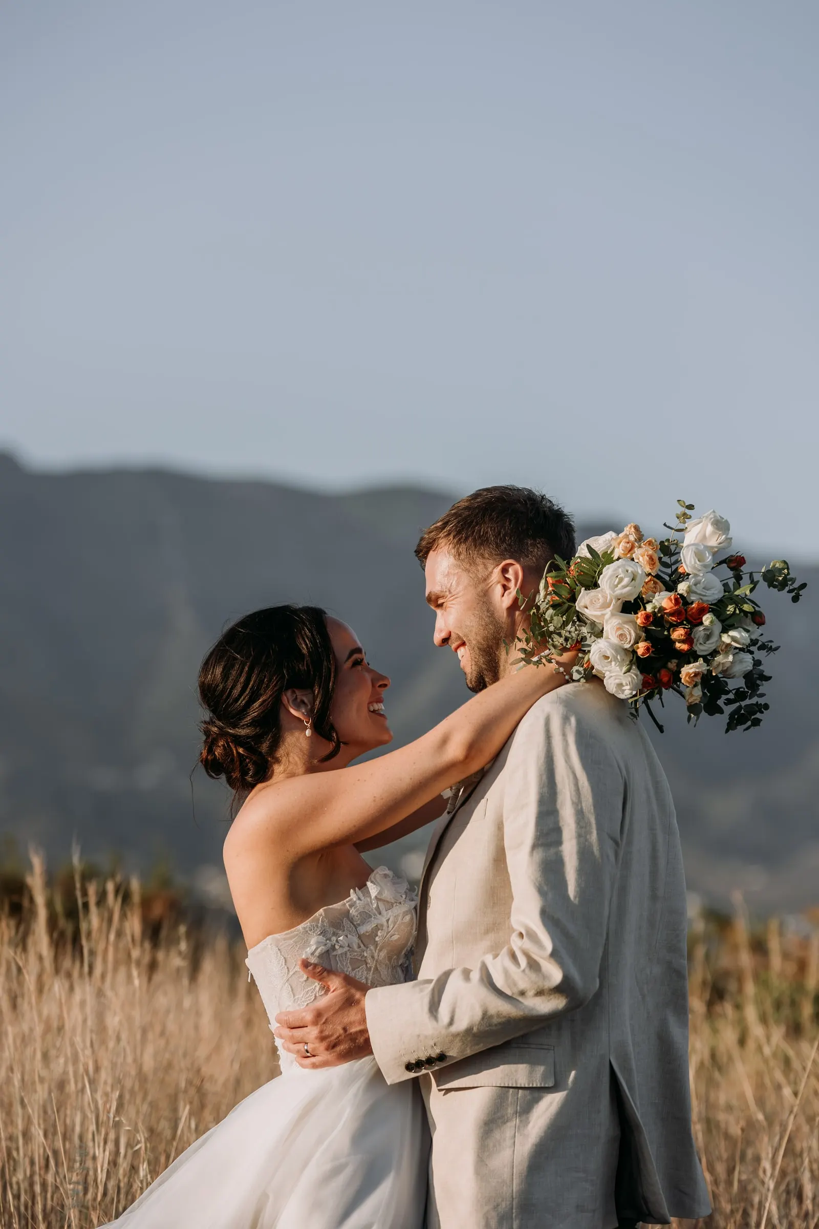 Bride with her arms around the groom's neck, bouquet in hand, golden hour in Mijas