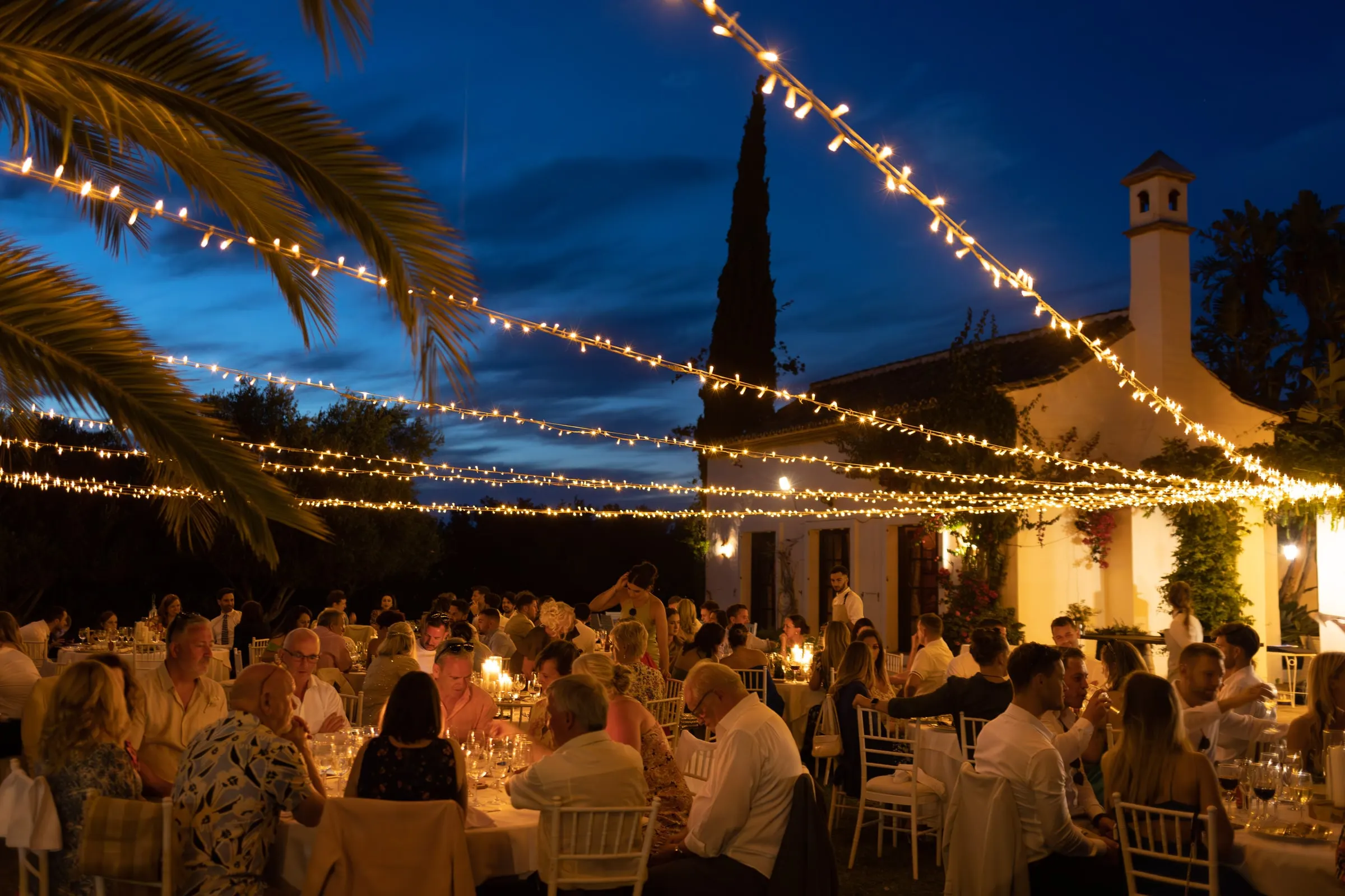 Dinner under fairy lights and palms at dusk, with the bell tower of Hacienda San José behind