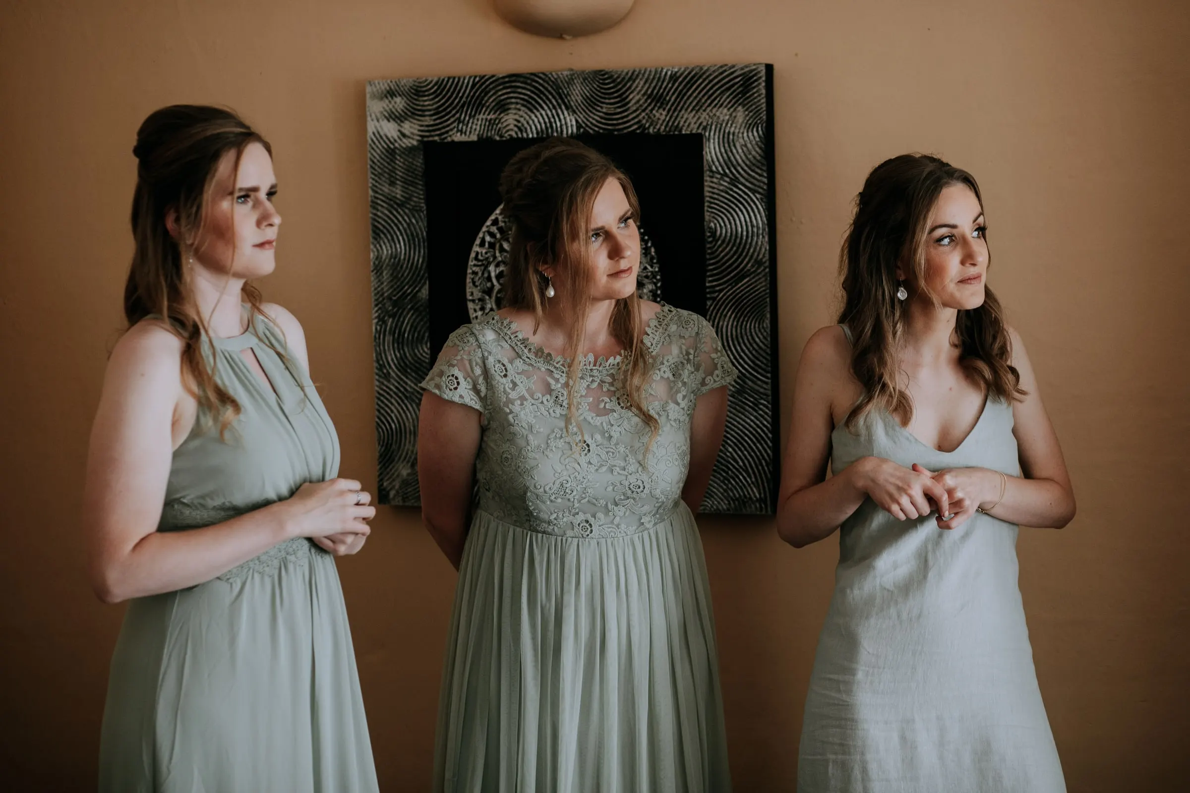 Three bridesmaids in sage green dresses waiting quietly in a warm-toned room, Hacienda San José, Mijas