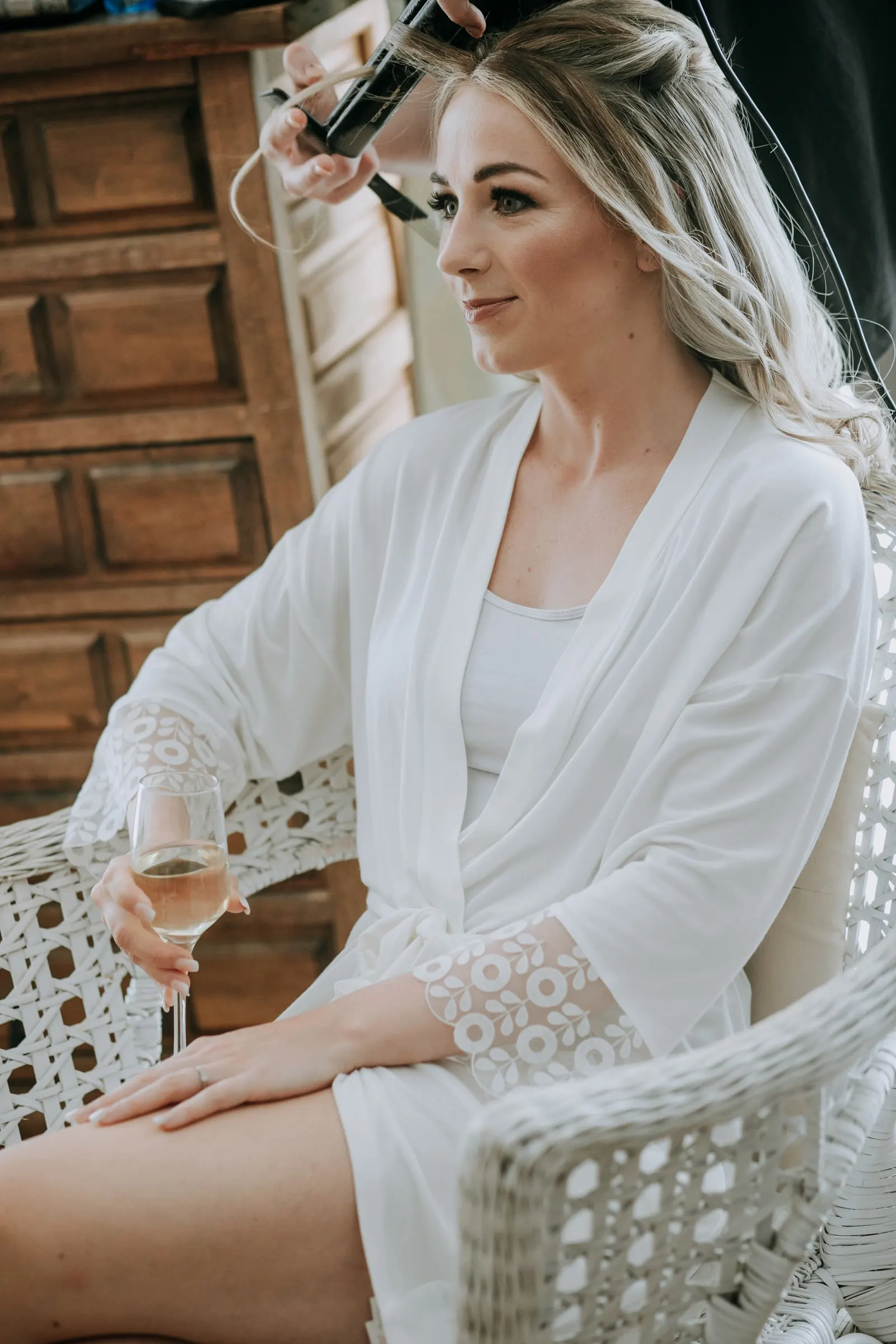 Bride in a white robe with a glass of wine as her hair is styled, Hacienda San José, Mijas