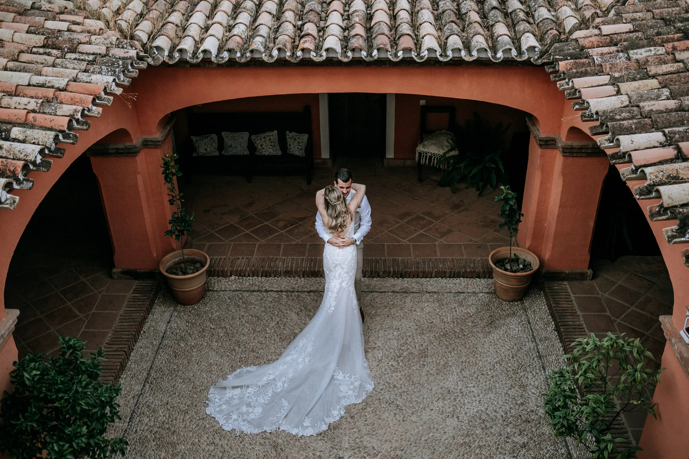Bride and groom embracing in the terracotta courtyard seen from above, her train spread out, Hacienda San José, Mijas