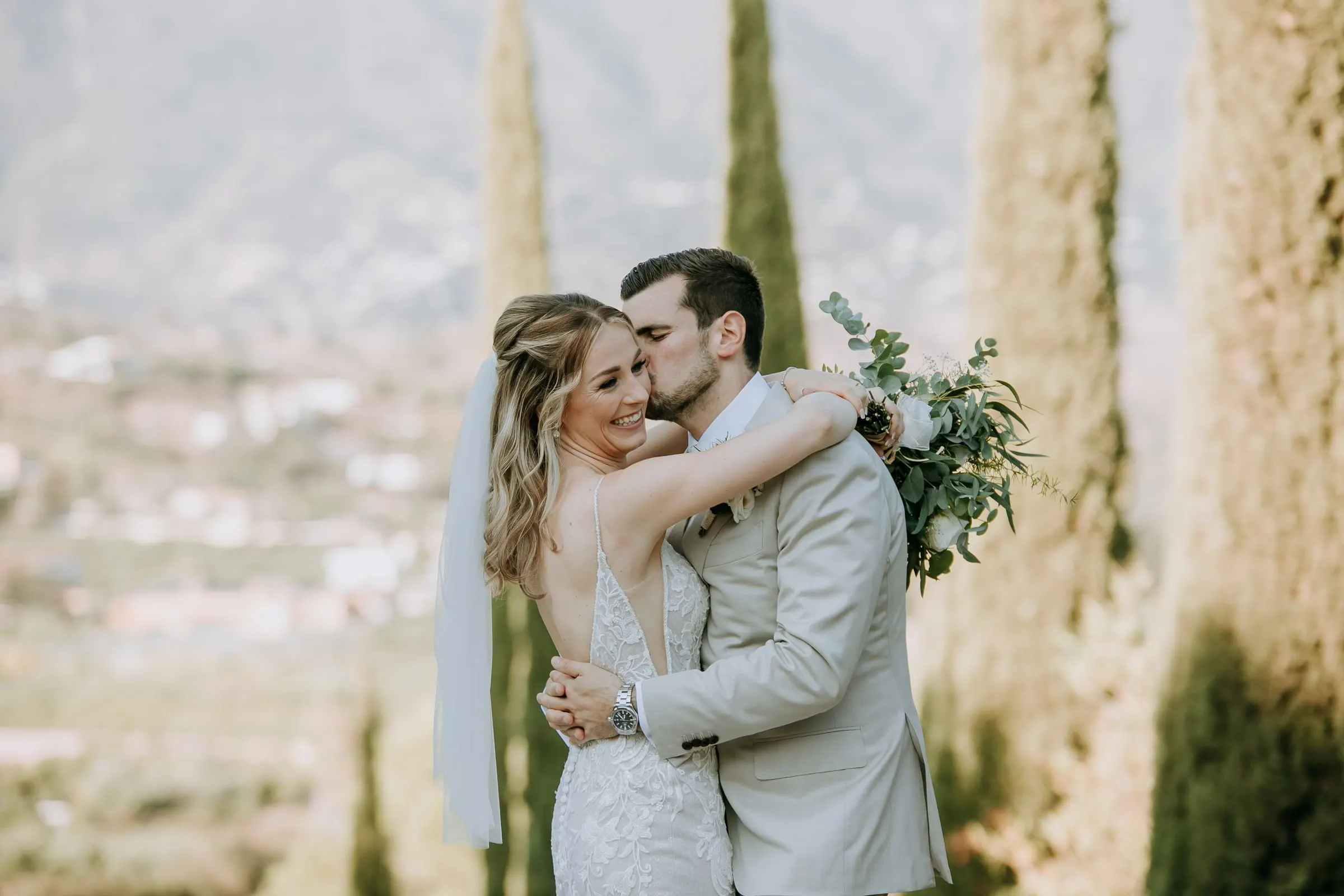 Groom kissing the bride's cheek as she smiles, cypresses and the valley behind, Hacienda San José, Mijas