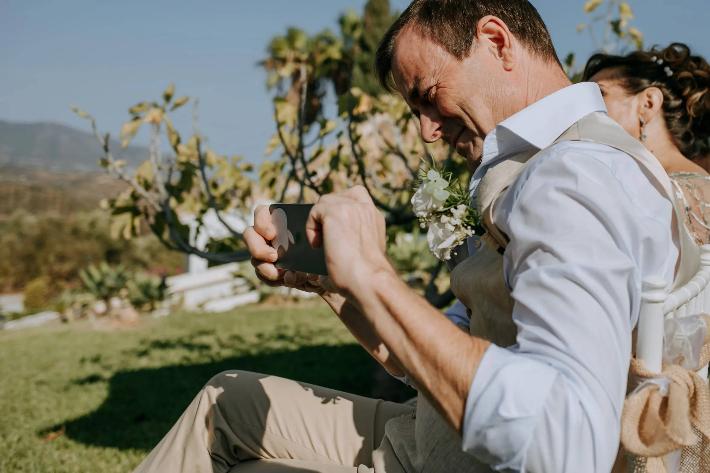 Smiling guest in a waistcoat filming the ceremony on his phone, Hacienda San José, Mijas