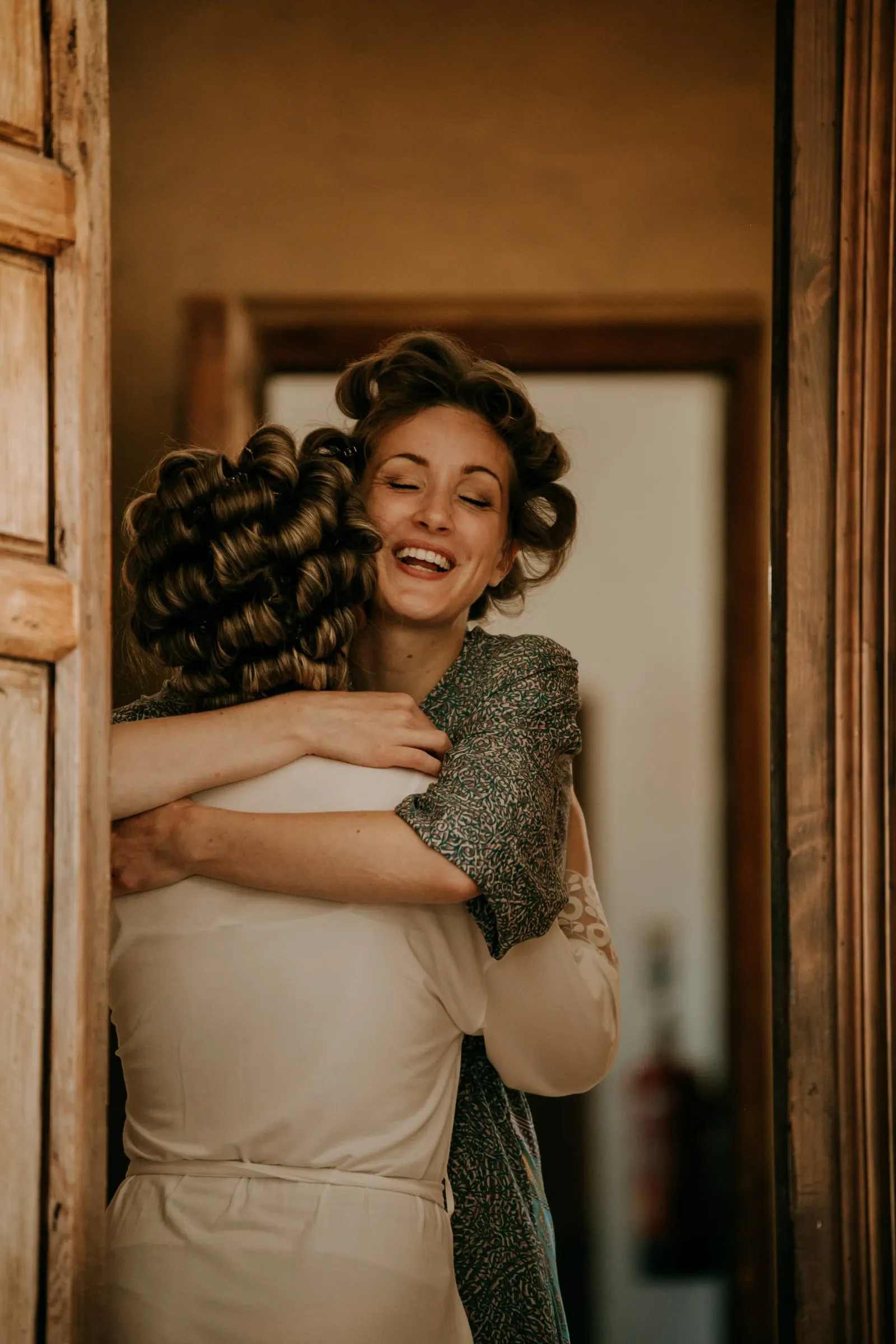 Two women in hair rollers sharing a warm hug in a wooden doorway, Hacienda San José, Mijas