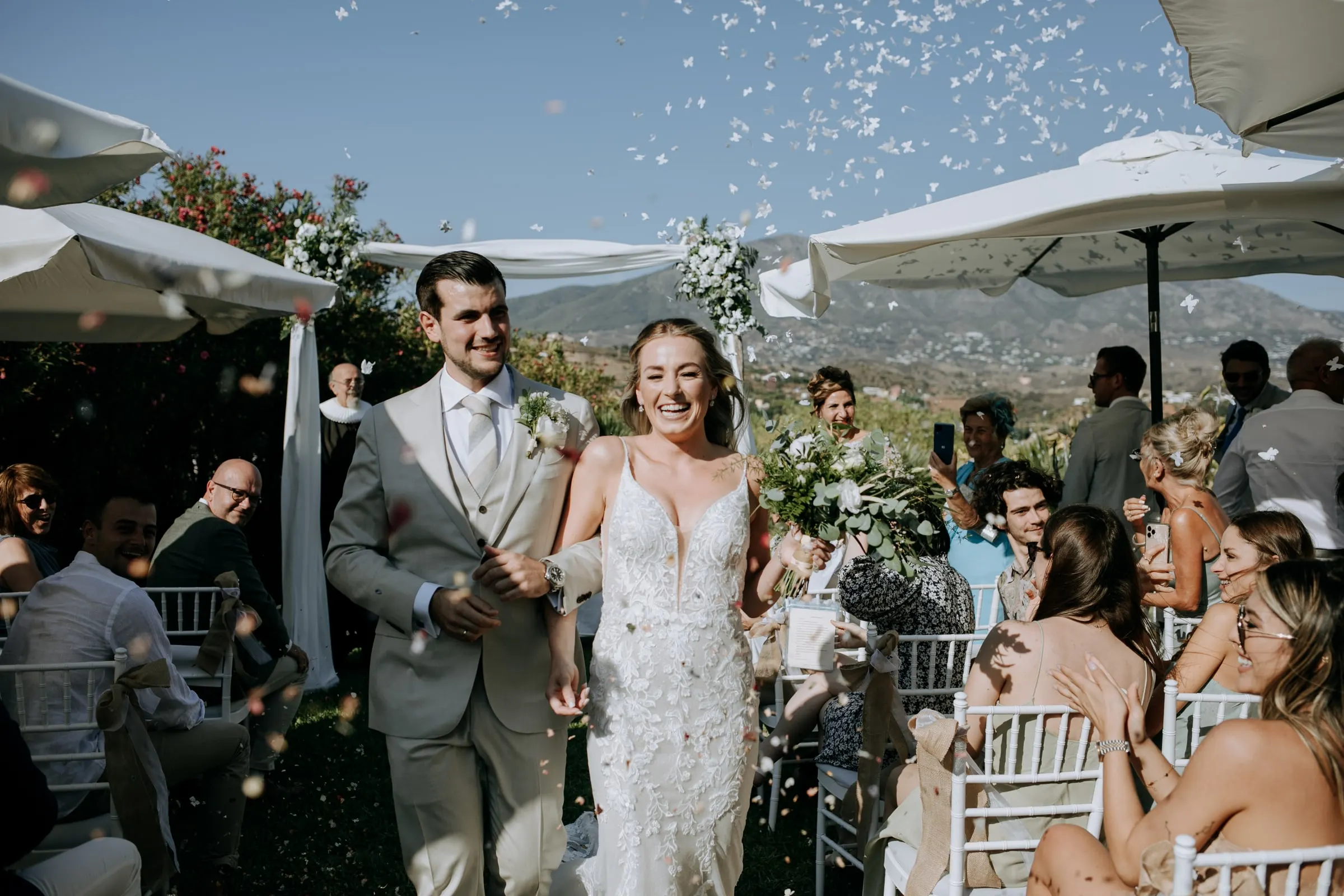 Bride and groom walk back down the aisle through a shower of confetti, guests cheering, Hacienda San José, Mijas