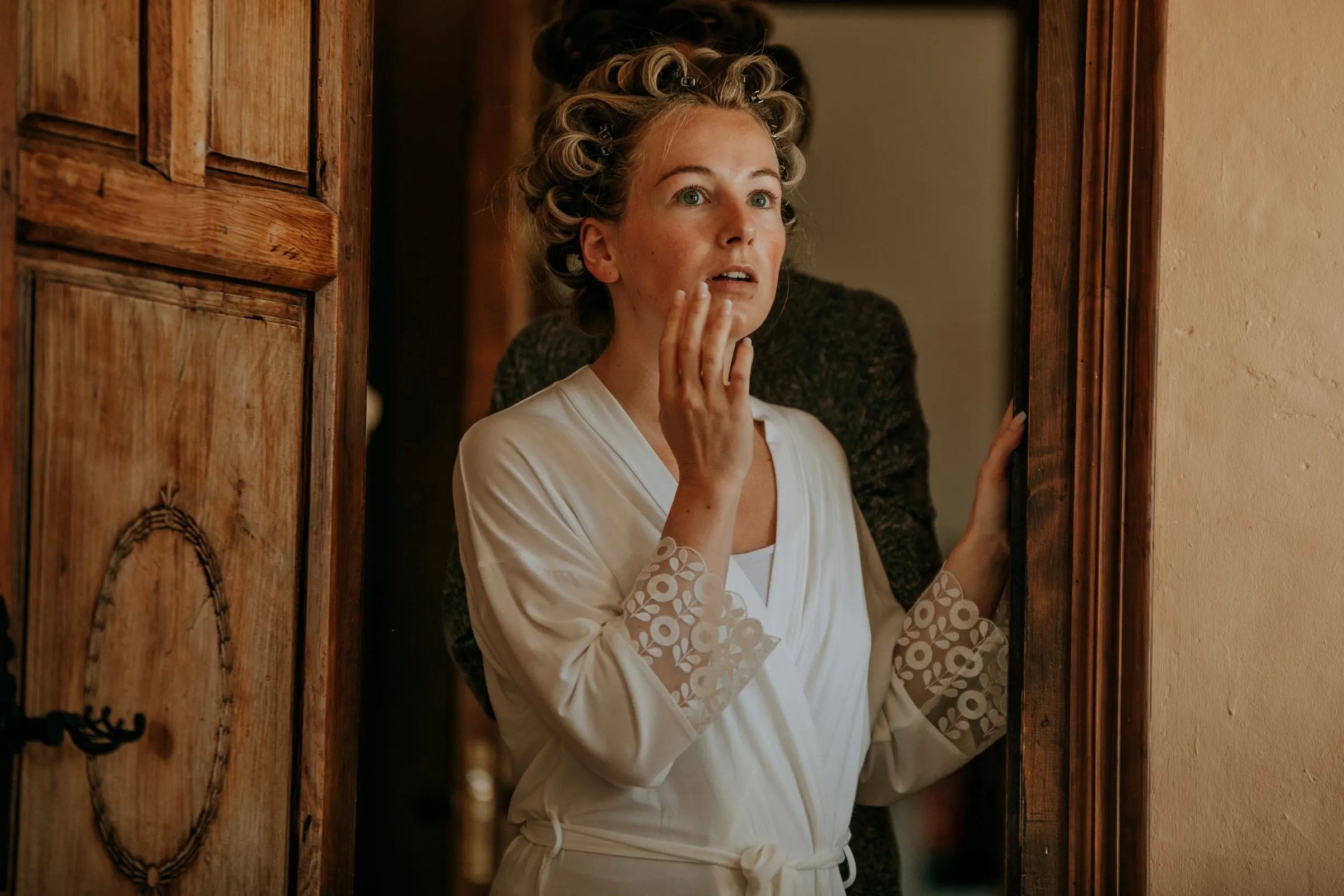 Woman in a robe and hair rollers peering emotionally around an old wooden door, Hacienda San José, Mijas