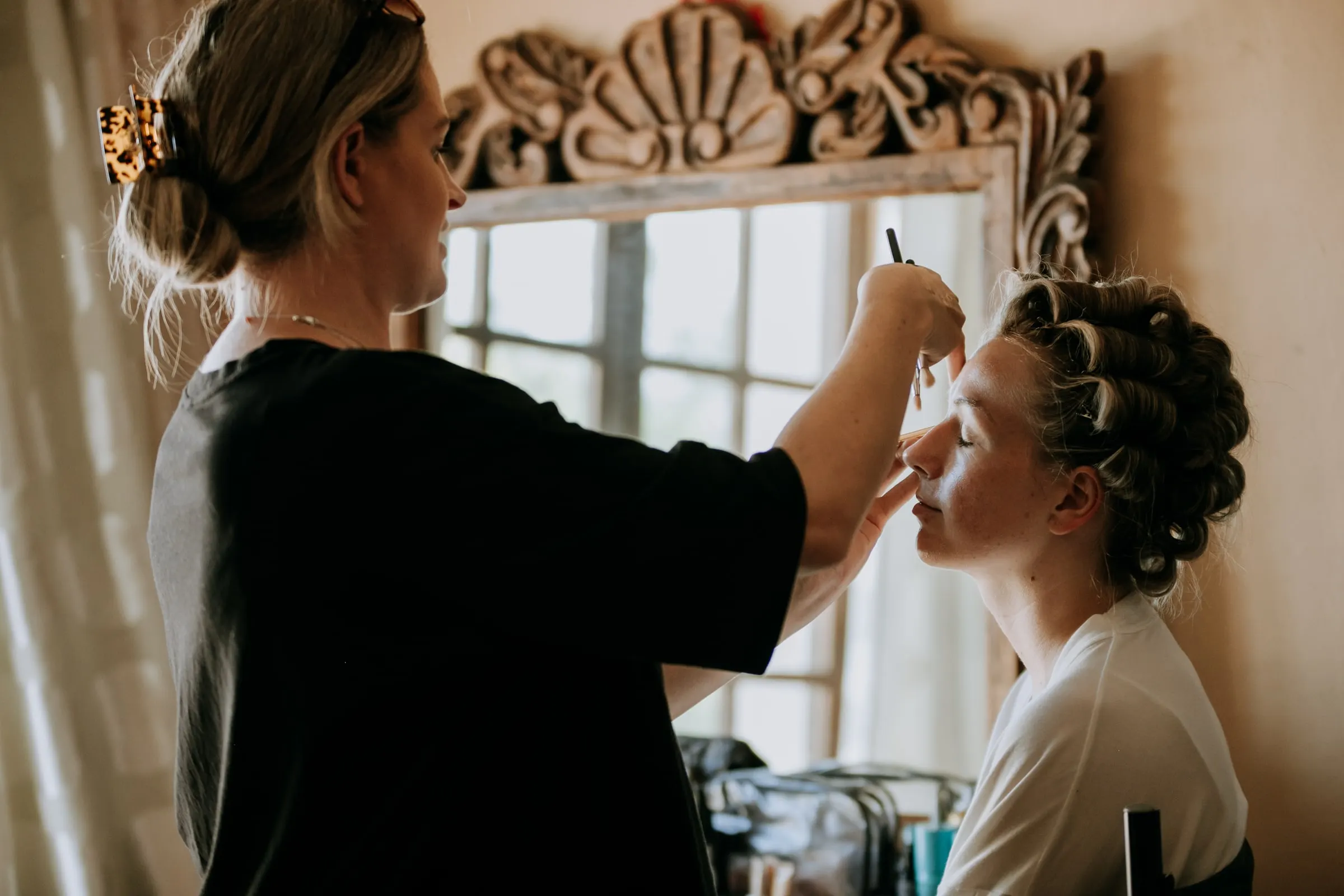 Make-up artist applying mascara to a woman in hair rollers before an ornate mirror, Hacienda San José, Mijas