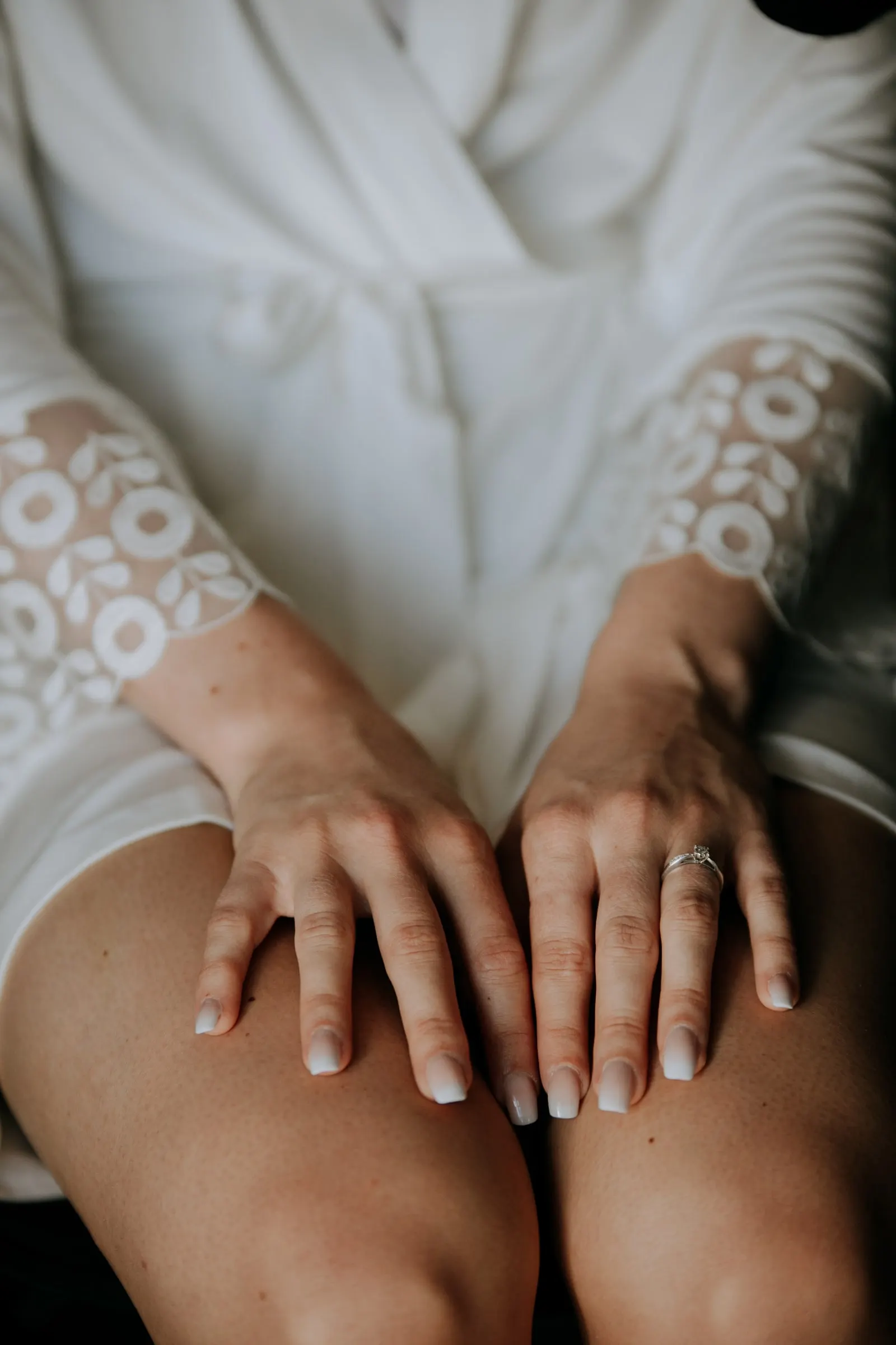 Detail of the bride's hands with her ring resting on her knees, lace robe sleeves, Hacienda San José, Mijas