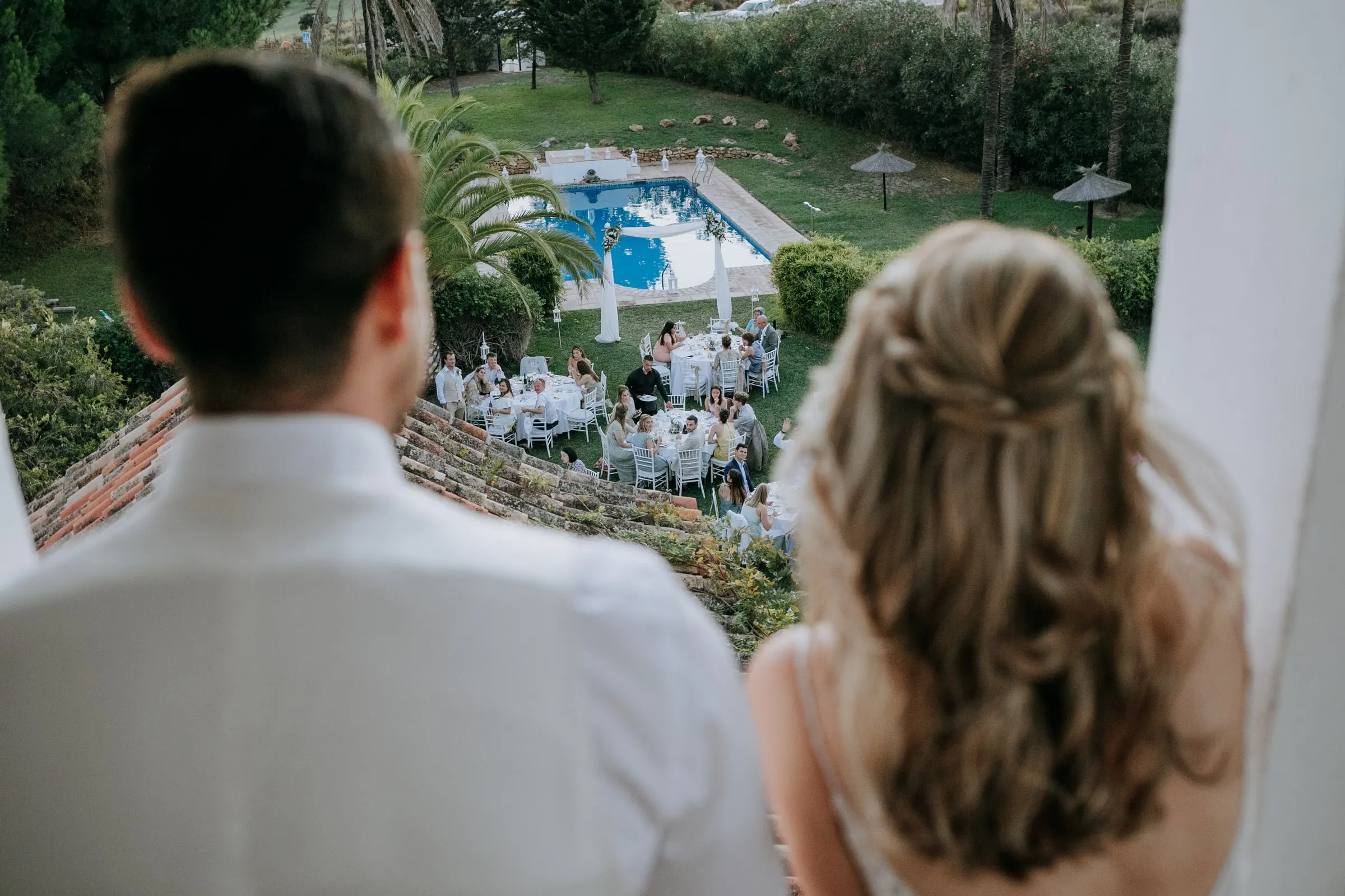Bride and groom looking down from a balcony at the tables set around the pool, Hacienda San José, Mijas