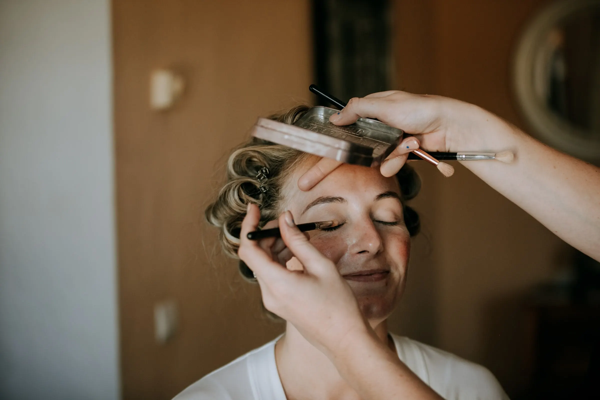 Close-up of a make-up artist's brush on the eyelid of a smiling woman in hair rollers, Hacienda San José, Mijas
