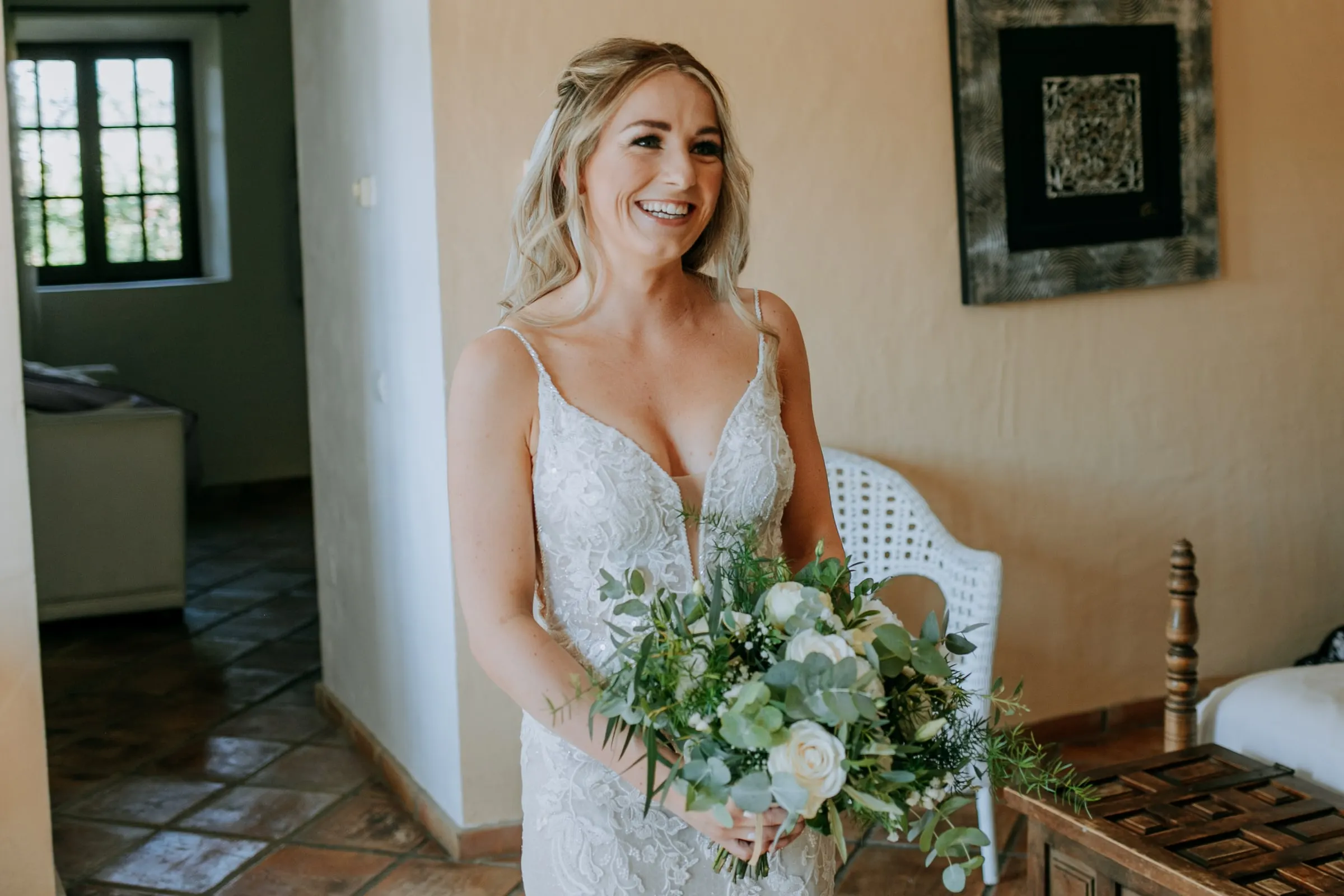 Bride in her lace gown with a green and white bouquet, smiling in the bedroom, Hacienda San José, Mijas