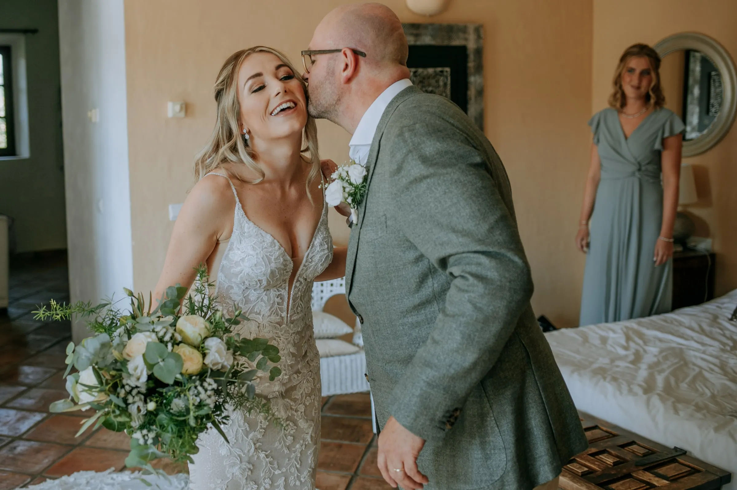 A man kisses the laughing bride on the cheek in the bridal room, bridesmaid behind, Hacienda San José, Mijas