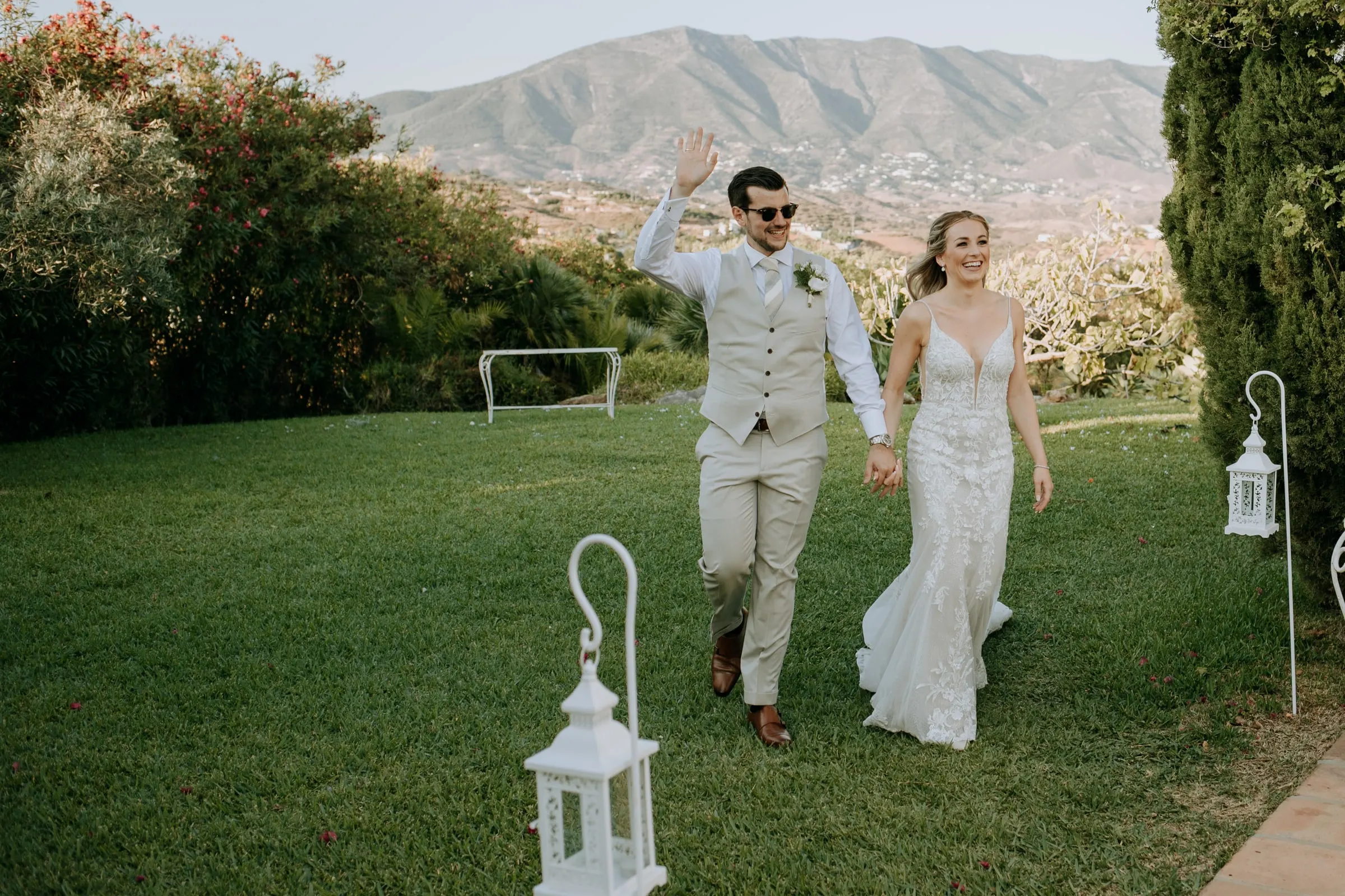 Groom waves as he walks with the bride across the lawn past white lanterns, Hacienda San José, Mijas