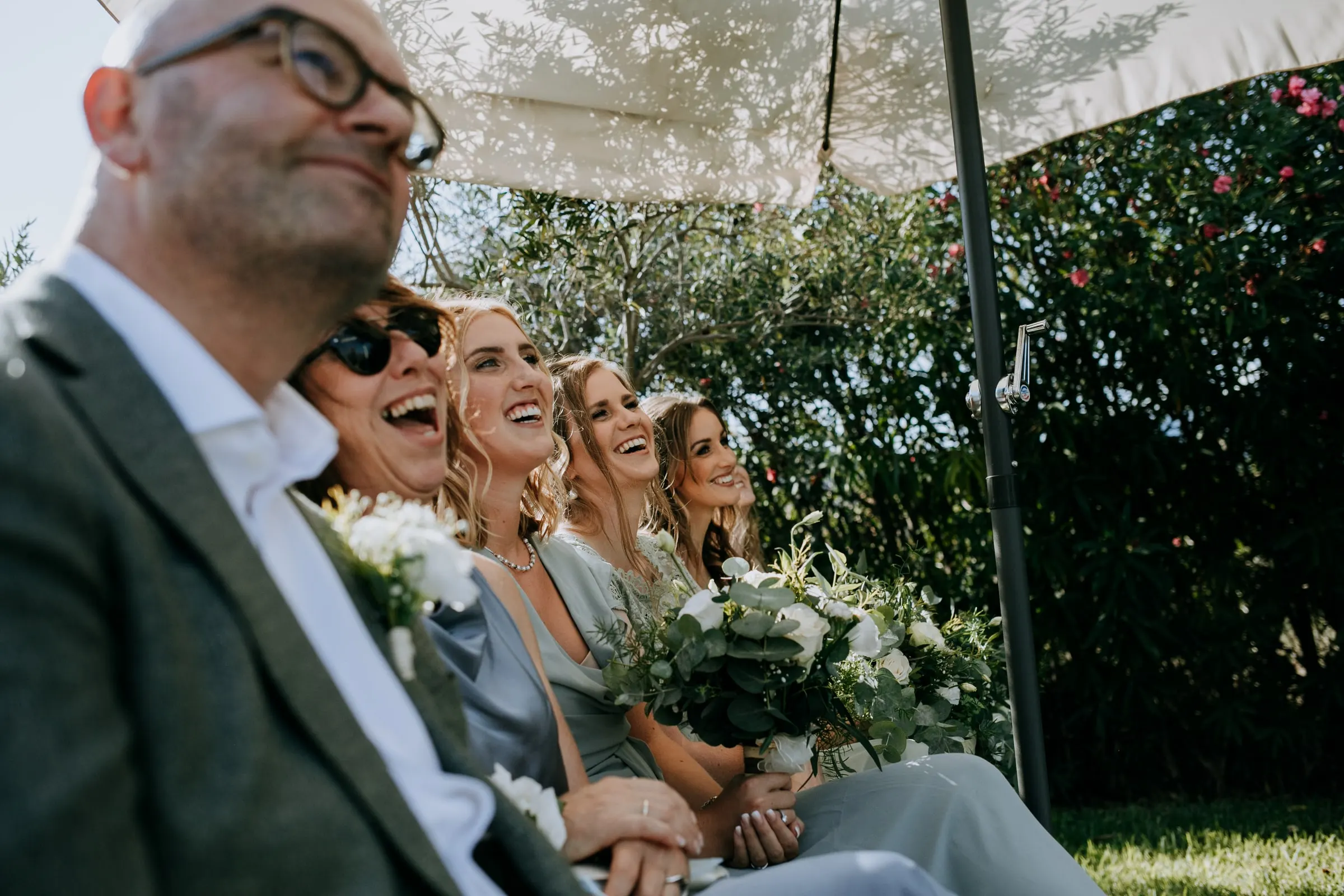 Guests and bridesmaids in the front row laughing during the ceremony, Hacienda San José, Mijas